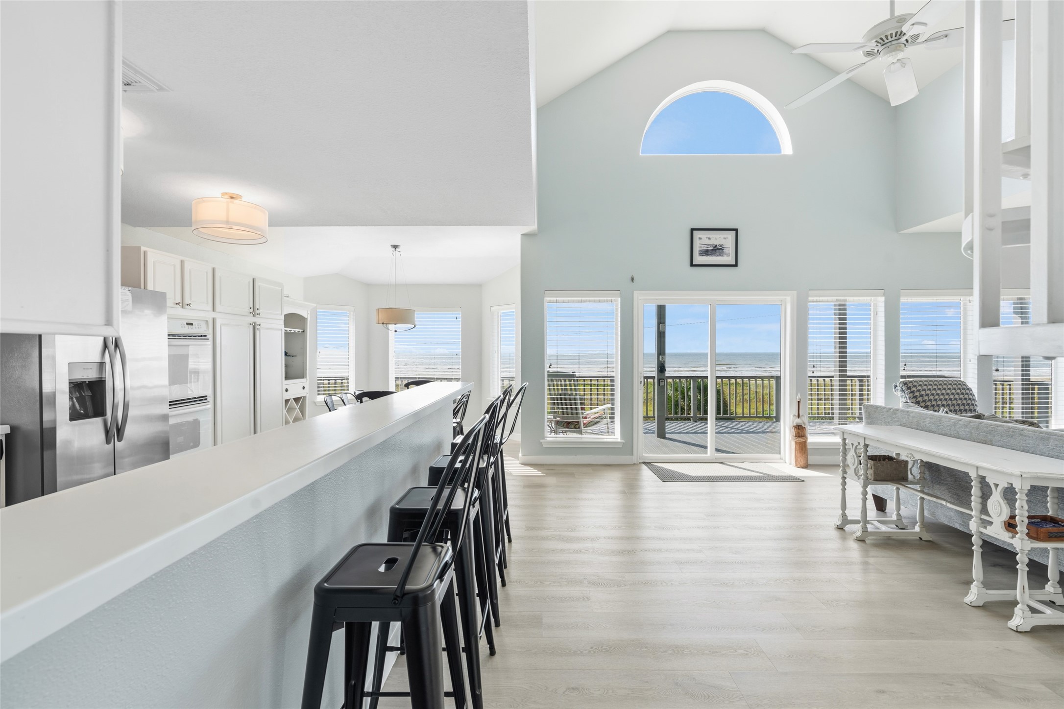 Open-concept living space with a vaulted ceiling, expansive ocean views through large windows, and a modern kitchen featuring a long breakfast bar.