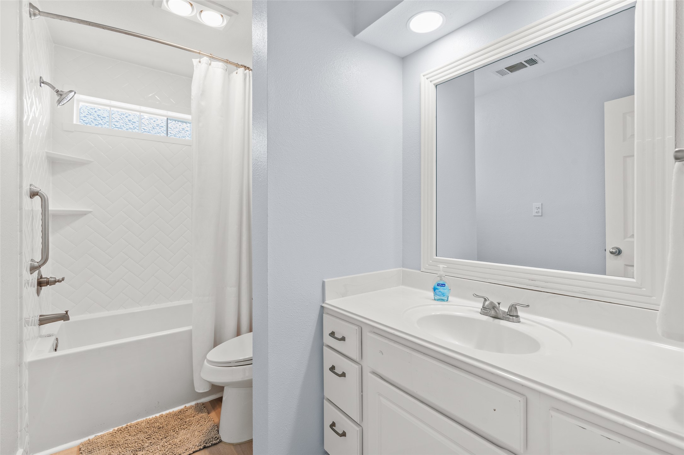 Bathroom featuring a white vanity, large mirror, and a classic bathtub with elegant herringbone tile detail.