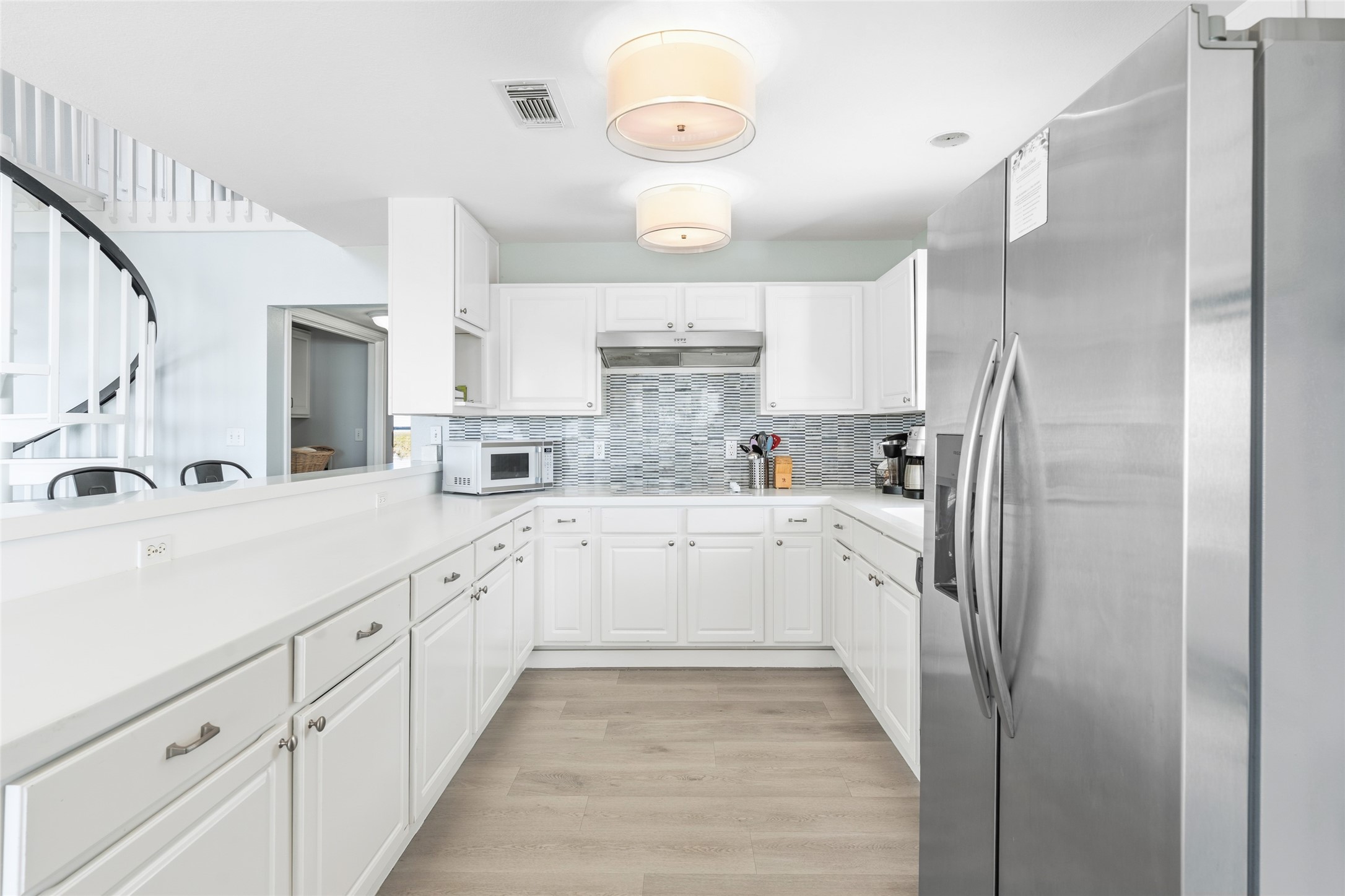 Bright and modern kitchen featuring sleek white cabinetry, stainless steel appliances, and a stylish tile backsplash, complemented by ample counter space and contemporary lighting.