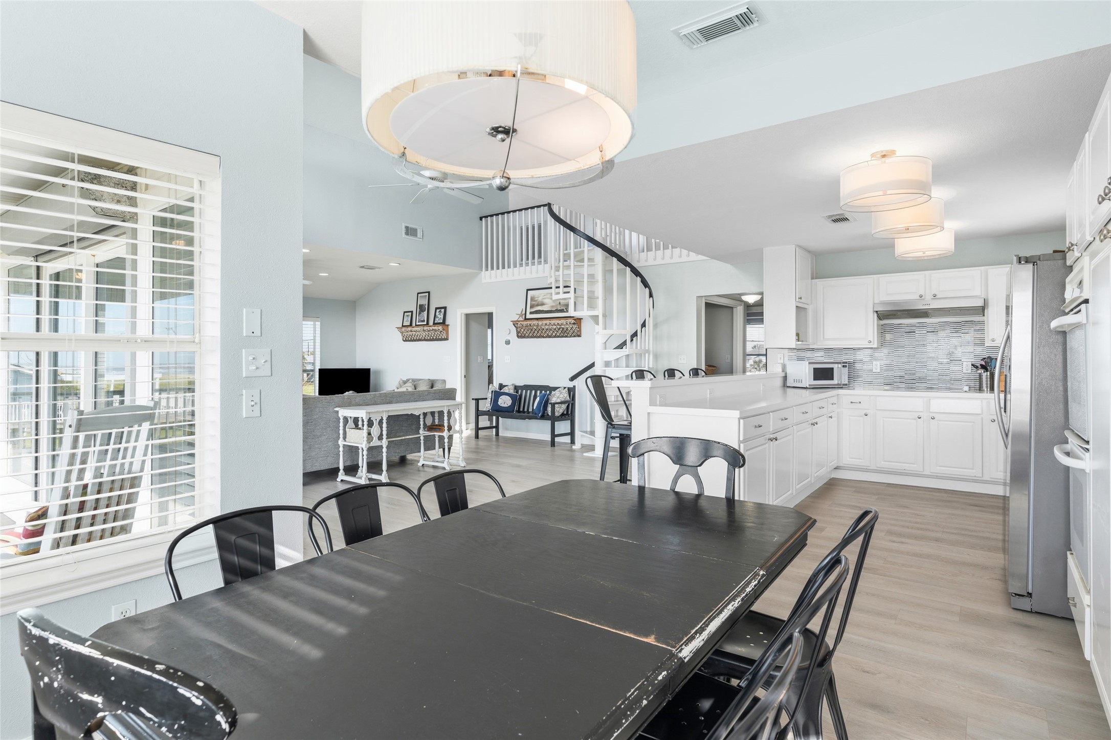 Open living space featuring a modern kitchen with coastal white cabinetry, a cozy dining area, and a stylish spiral staircase.