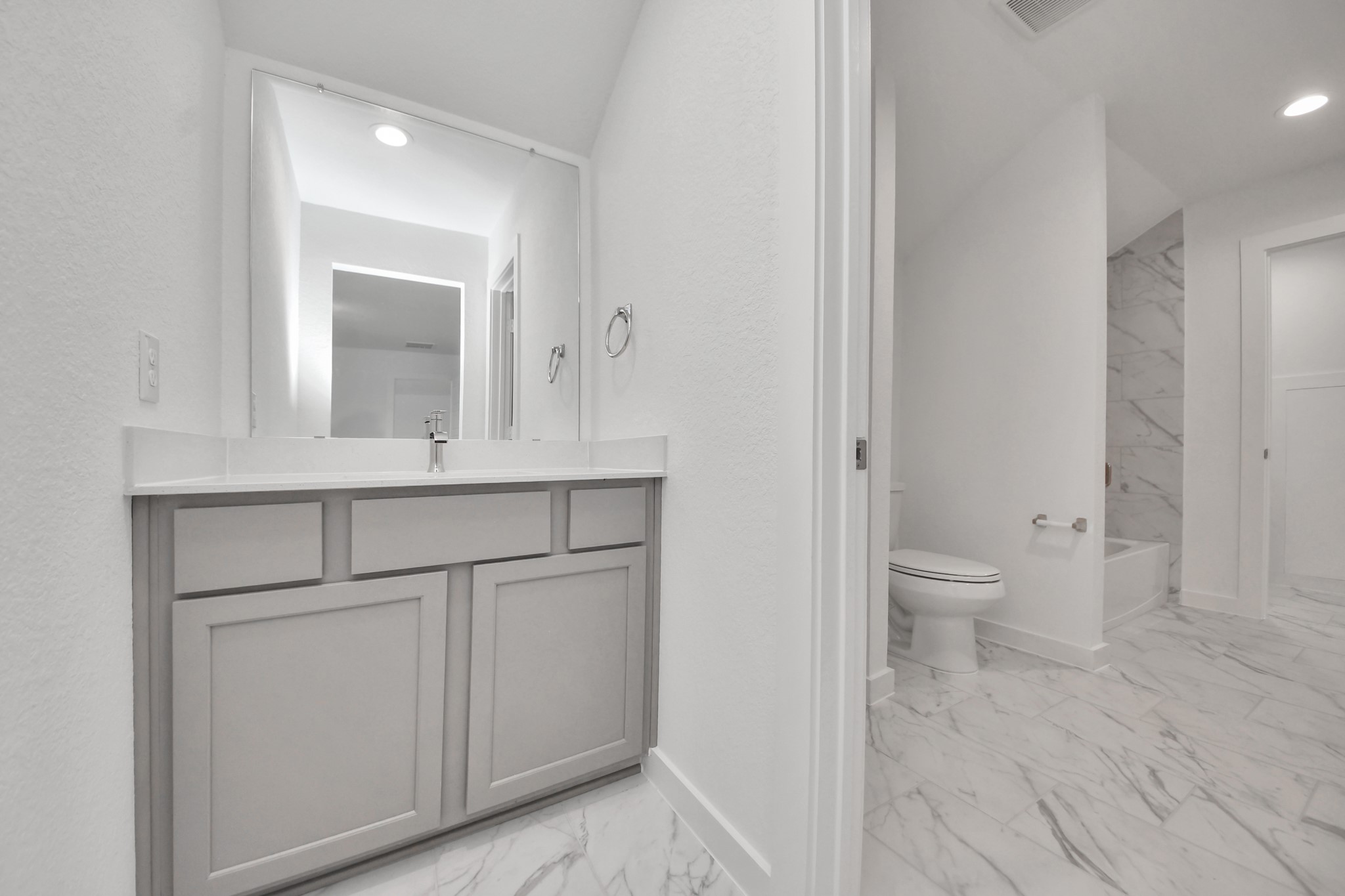 Experience convenience in the secondary bathroom, designed for Jack and Jill arrangements, now with a separate vanity area. This well-appointed space showcases stylish tile flooring, a bath/shower combo with an elegant tile surround, and light-stained wood cabinets. The beautiful light countertop adds a touch of sophistication, combining functionality and aesthetics seamlessly.