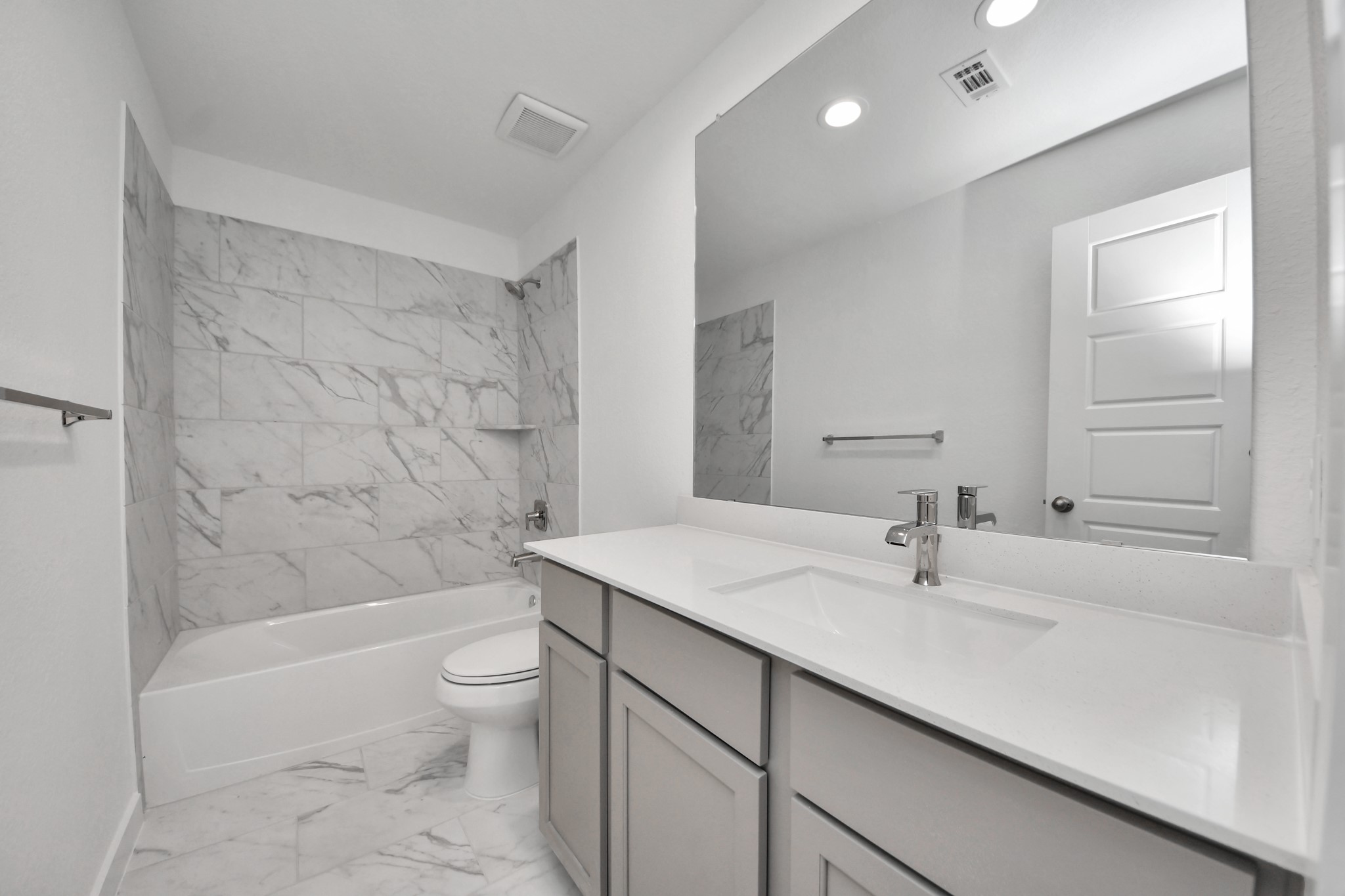 Secondary bath features tile flooring, bath/shower combo with tile surround, light stained wood cabinets, beautiful light countertop.