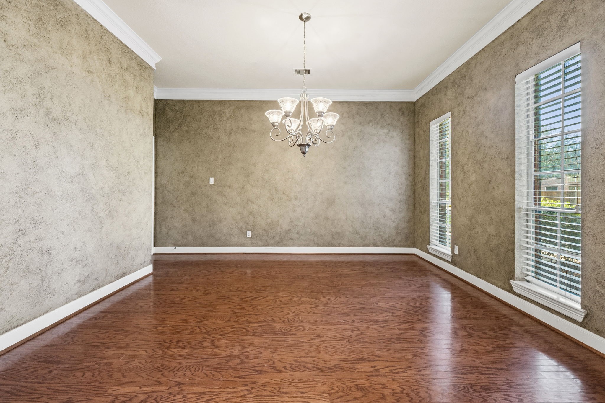 Elegant dining room with rich hardwood floors, textured walls, and a stylish chandelier. Large windows provide ample natural light, creating a warm and inviting atmosphere.