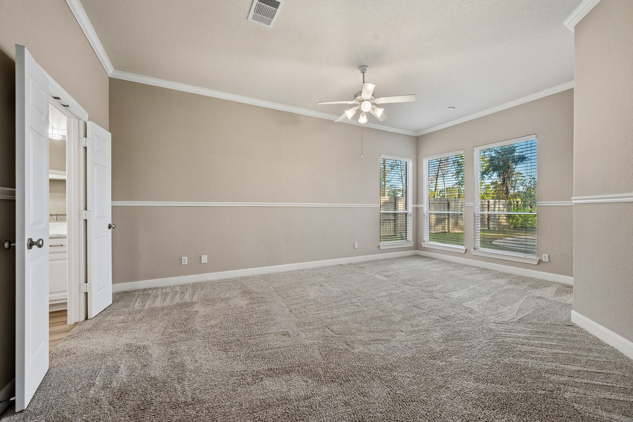 Spacious primary bedroom with neutral tones, featuring plush carpeting, crown molding, and large windows for abundant natural light.
