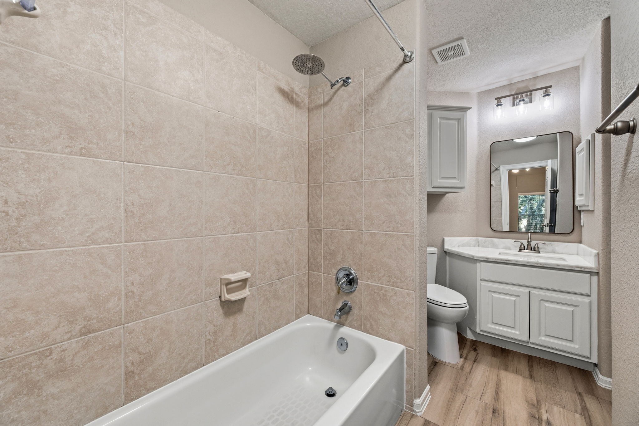 Modern bathroom featuring a tiled shower and bathtub combo, elegant vanity with ample storage, and contemporary fixtures, complemented by warm wood-style flooring.