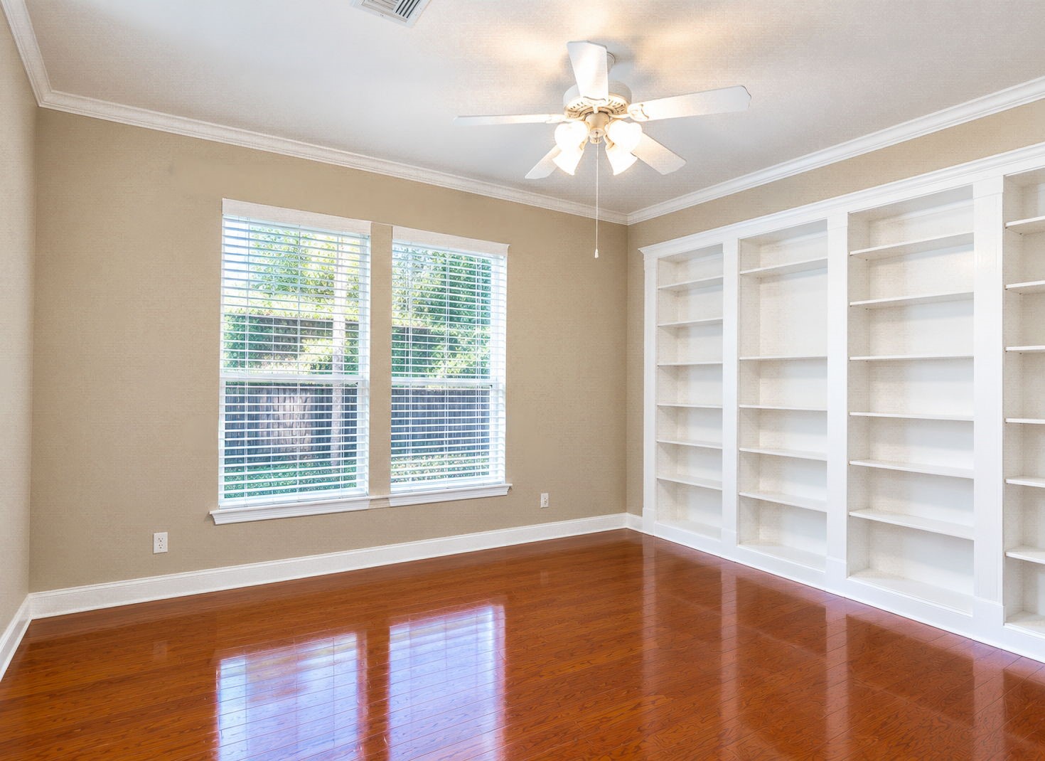 French doors leading to this study featuring elegant built-in shelving, warm hardwood floors, and ample natural light from large windows.