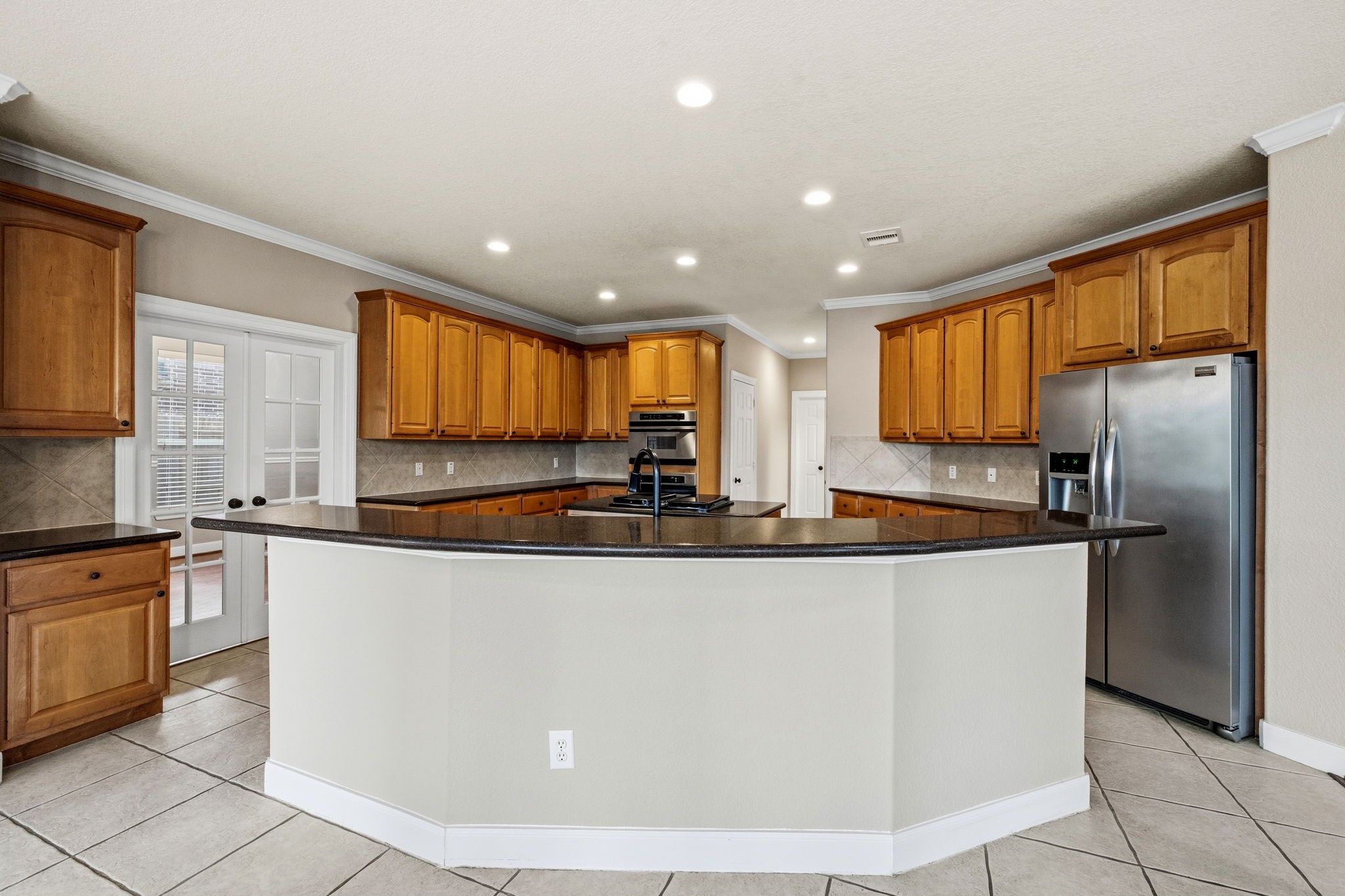 Spacious kitchen with a large curved island, granite countertops, stainless steel appliances, and ample wooden cabinetry.