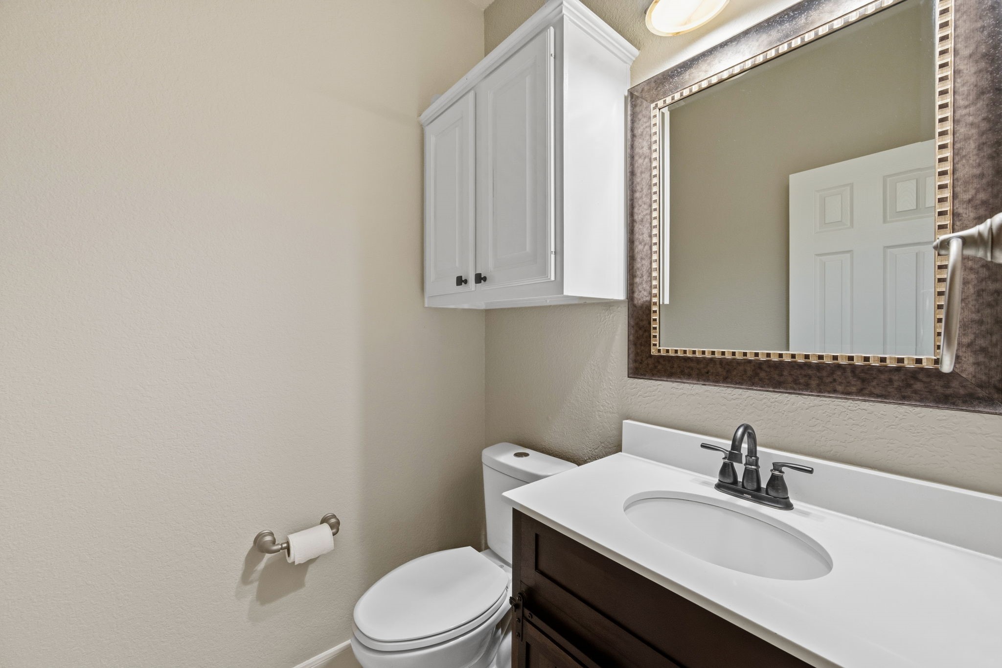 Charming powder room featuring a sleek vanity with a modern faucet, a stylish framed mirror, and convenient overhead cabinetry for extra storage.