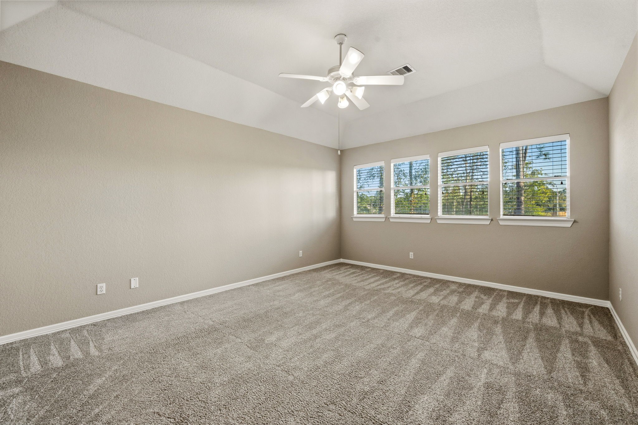 Spacious gameroom with plush carpet, large windows for natural light, and a modern ceiling fan, offering a cozy and inviting atmosphere.