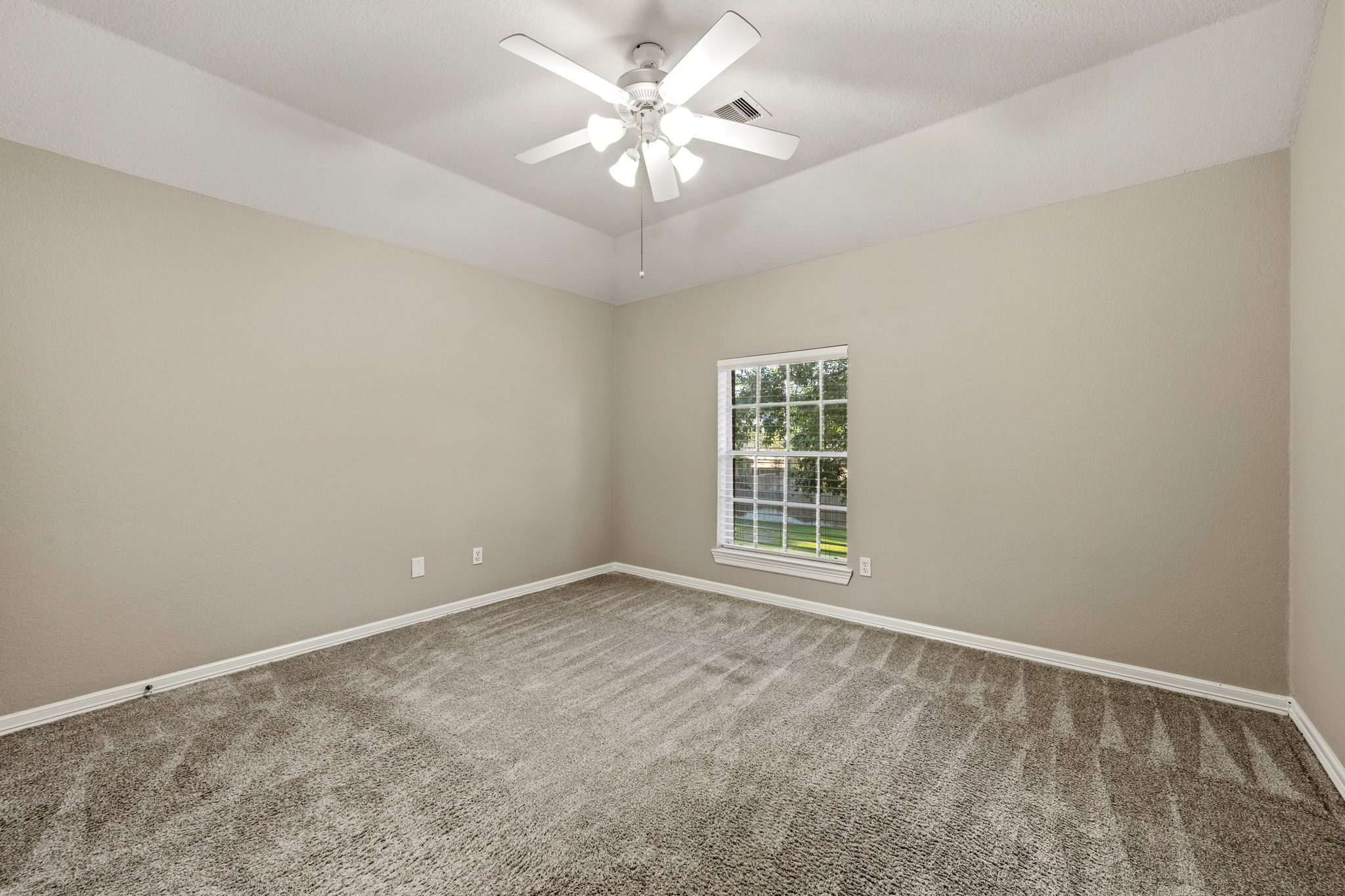 Spacious bedroom with plush carpeting and a large window for natural light, complemented by a ceiling fan for comfort.