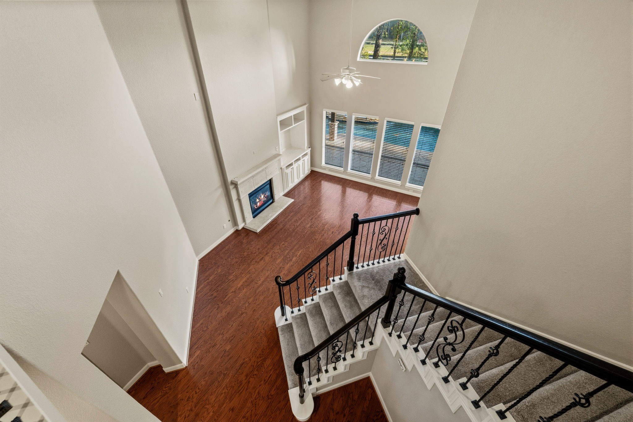 Stunning two-story living area with elegant staircase, rich wood floors, a cozy fireplace, and abundant natural light from expansive windows overlooking the backyard.