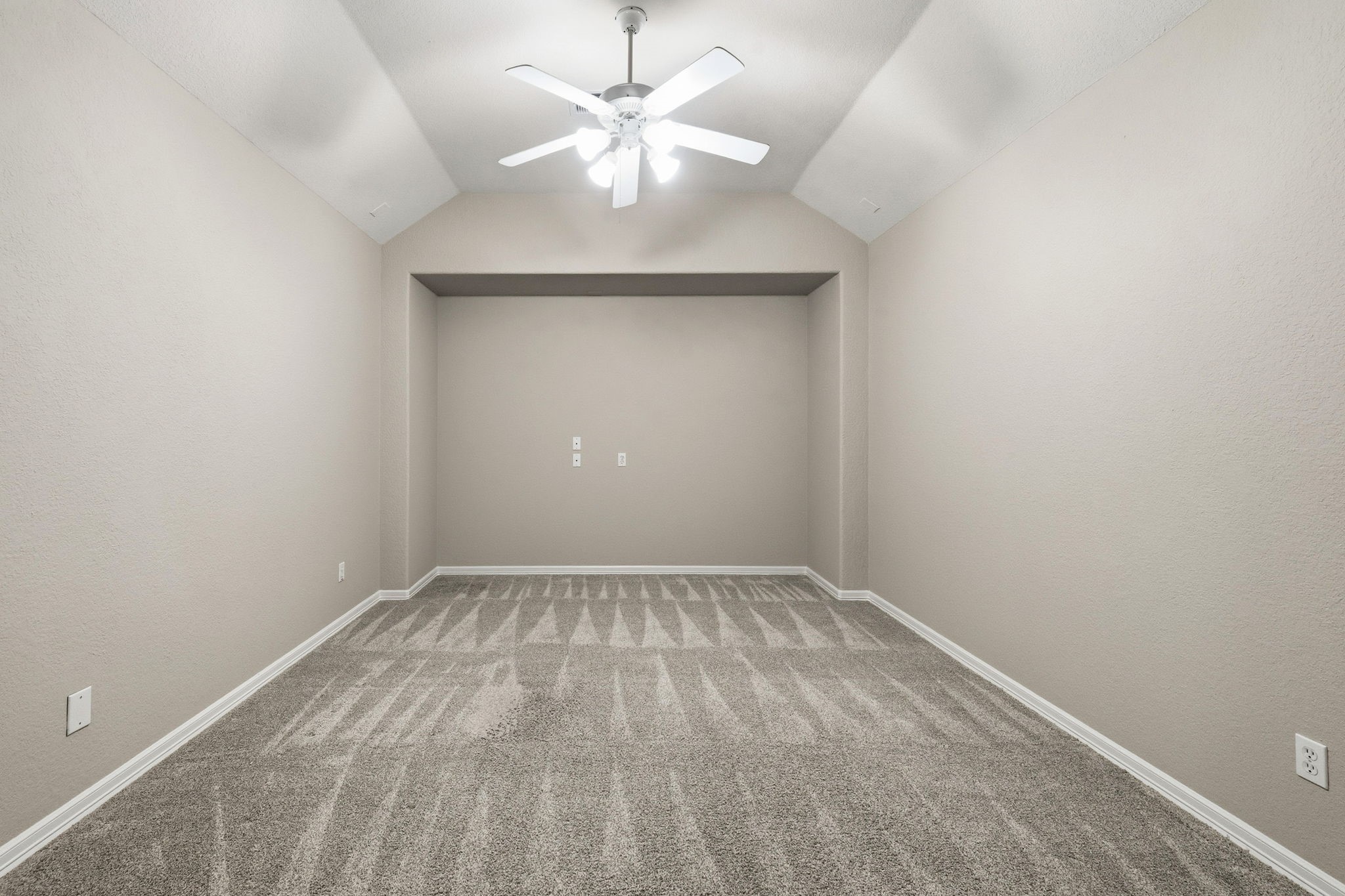 Spacious media room with vaulted ceiling, neutral walls, plush carpet, and a ceiling fan.
