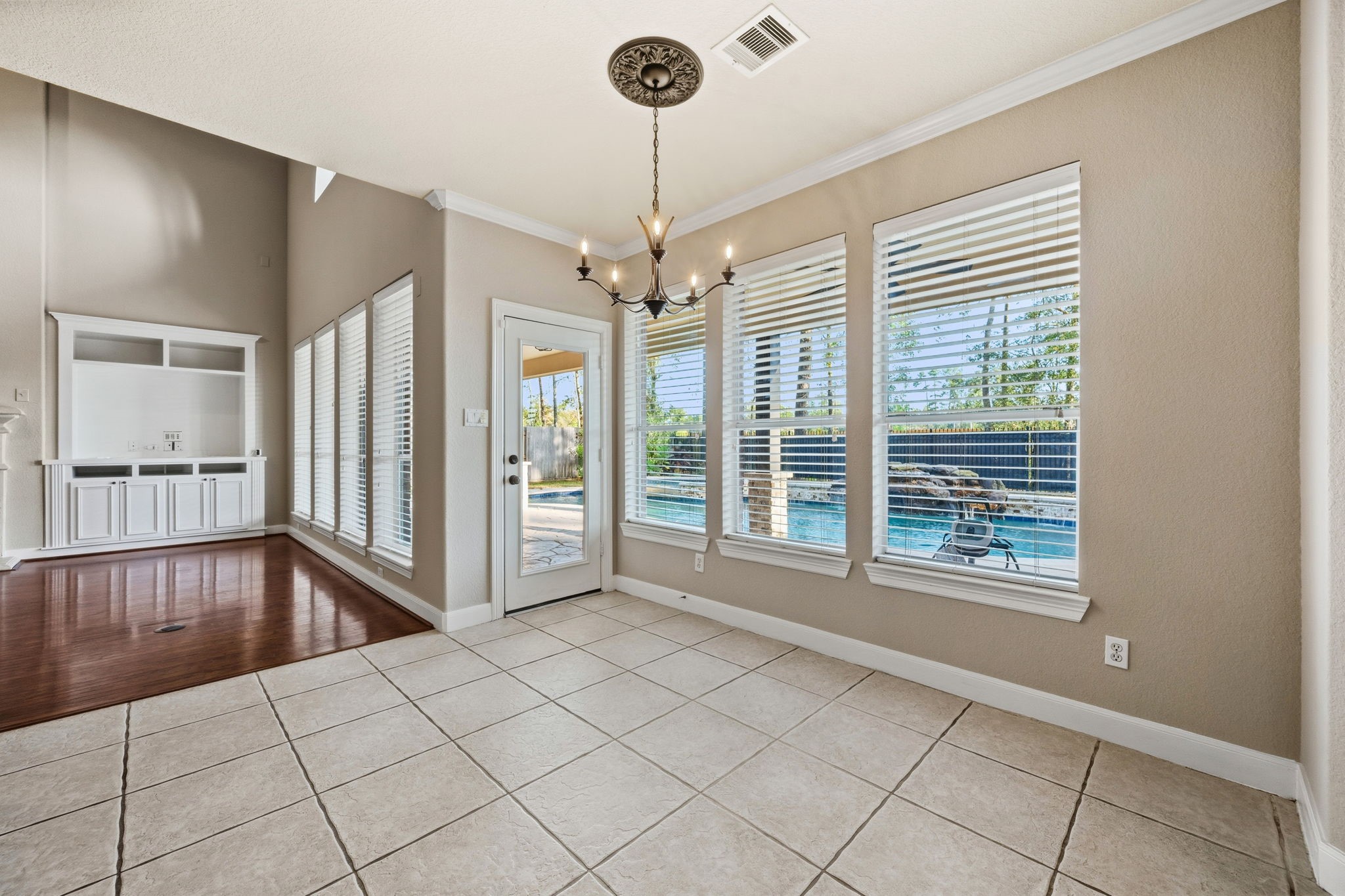 Bright dining area with tile flooring, adjacent to the living space and leading to backyard. Large windows and a glass door provide views of the inviting pool and patio.