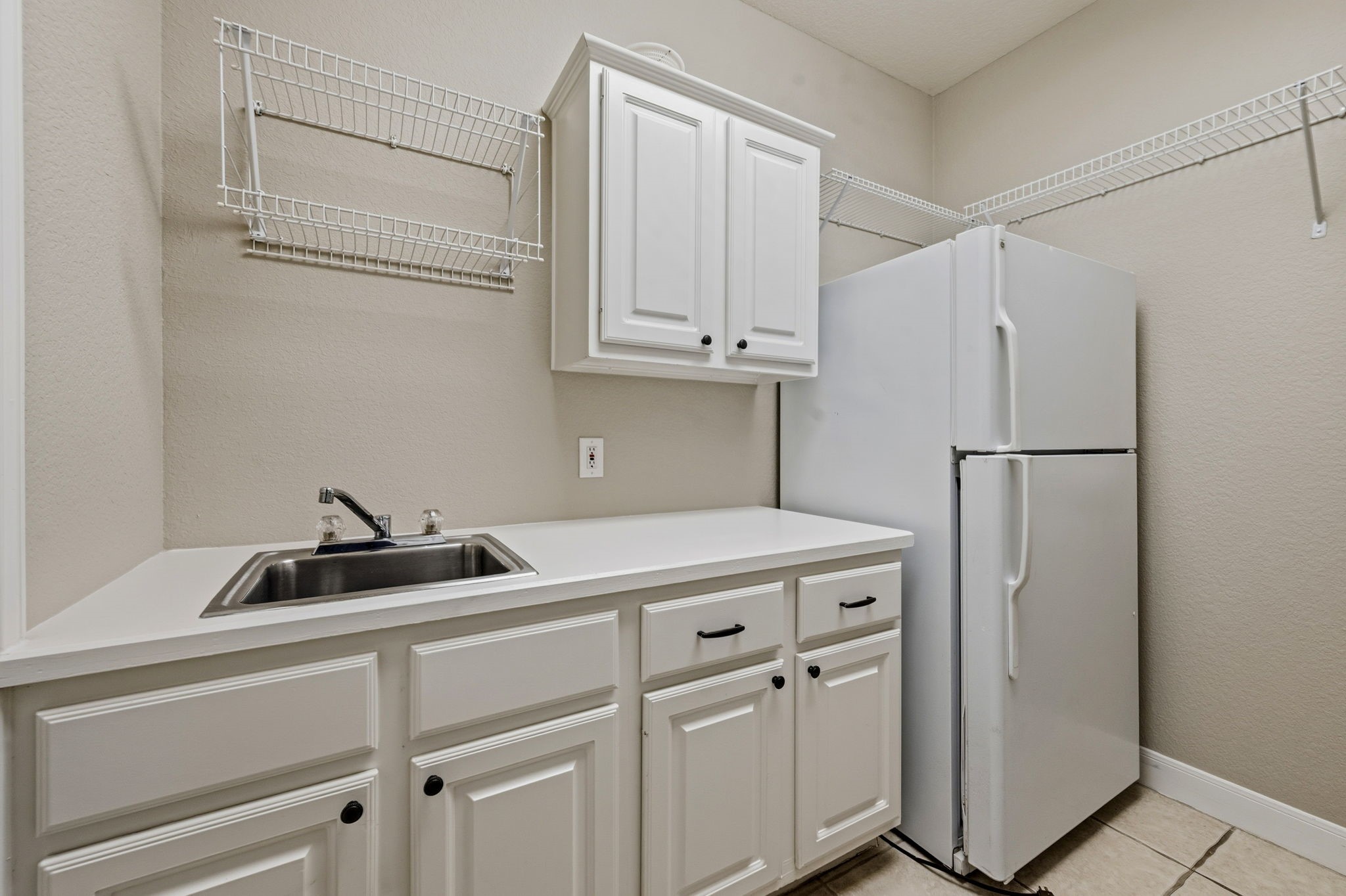 Spacious utility room featuring ample cabinetry, a sink, and a full-size refrigerator, complemented by convenient wire shelving for extra storage.