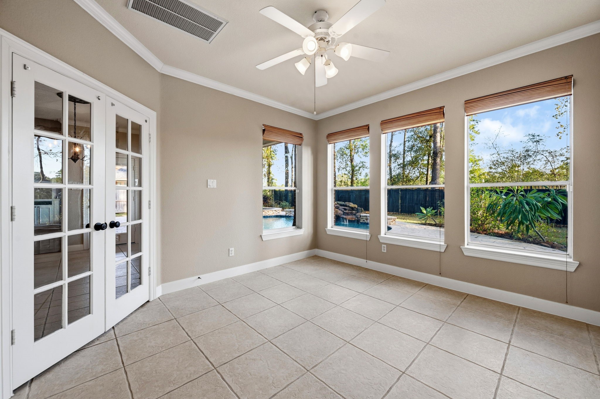Bright sunroom with tile flooring, ceiling fan, and large windows offering serene views of the backyard and pool. French doors add elegance and connect to the rest of the home.
