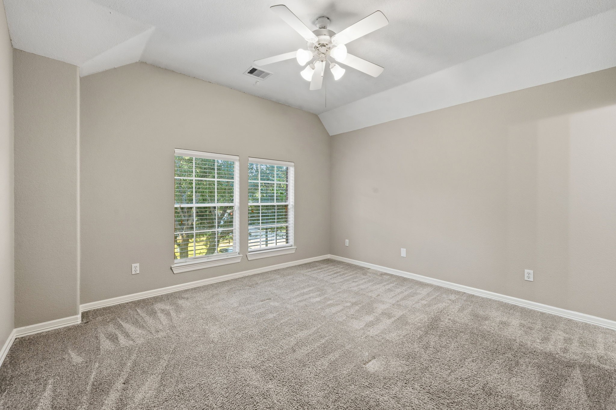 Spacious and bright bedroom with neutral walls, plush carpeting, and large windows letting in natural light, complemented by a ceiling fan for added comfort.