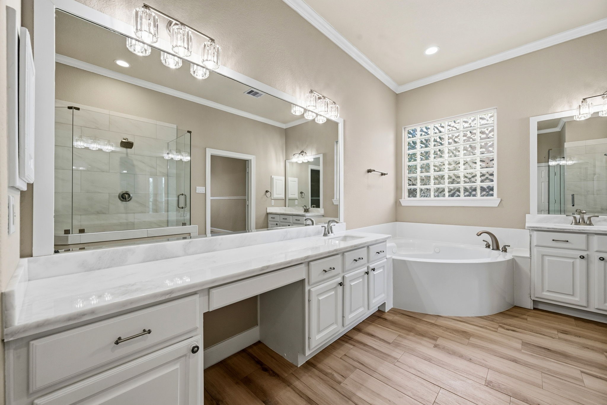 Elegant bathroom featuring a spacious vanity with dual sinks, a luxurious soaking tub, and a glass-enclosed shower, all accented by chic lighting and warm wood-like flooring.