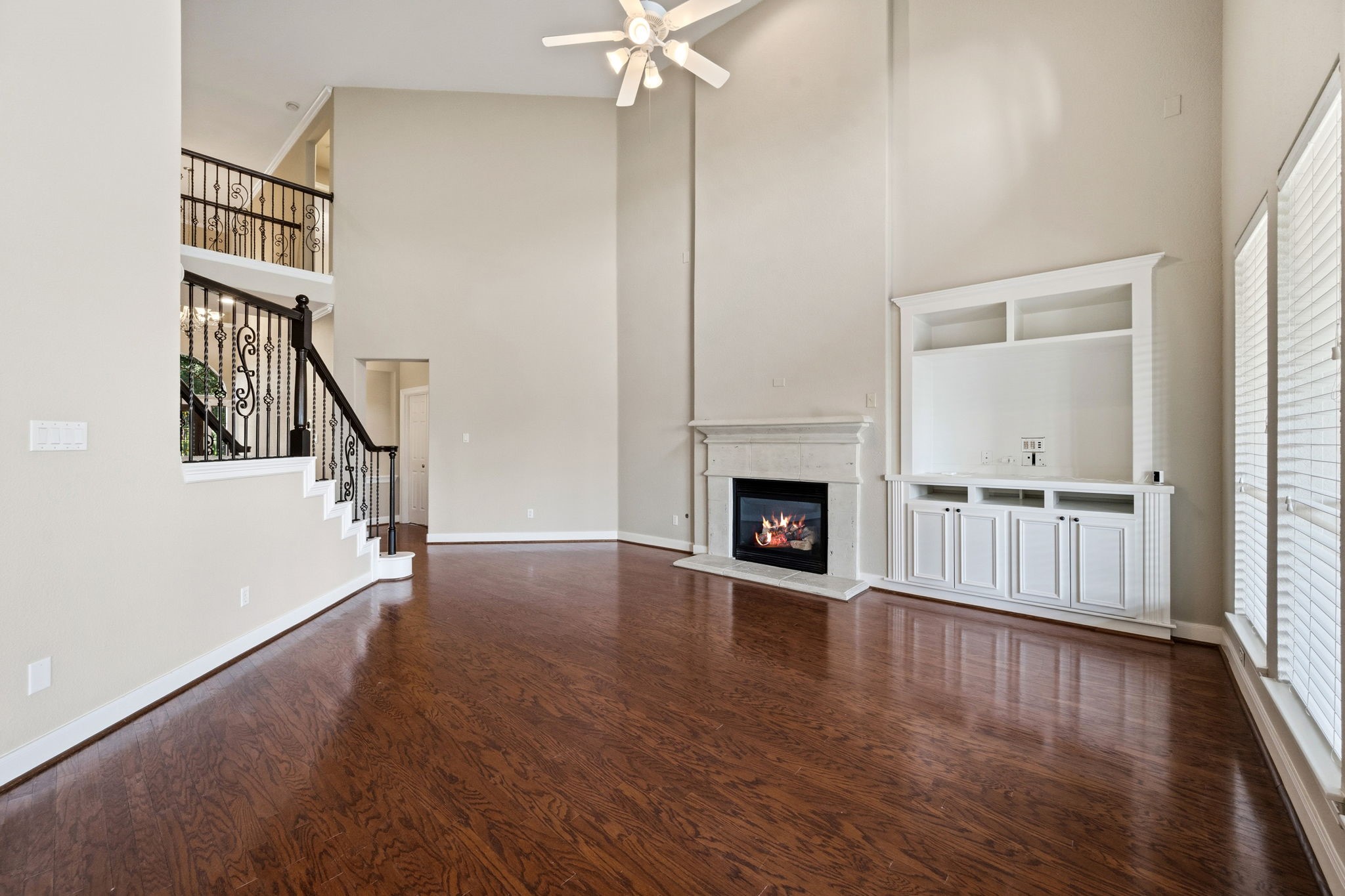 Spacious living room with soaring ceilings, elegant staircase, a cozy fireplace, built ins and abundant natural light from large windows.