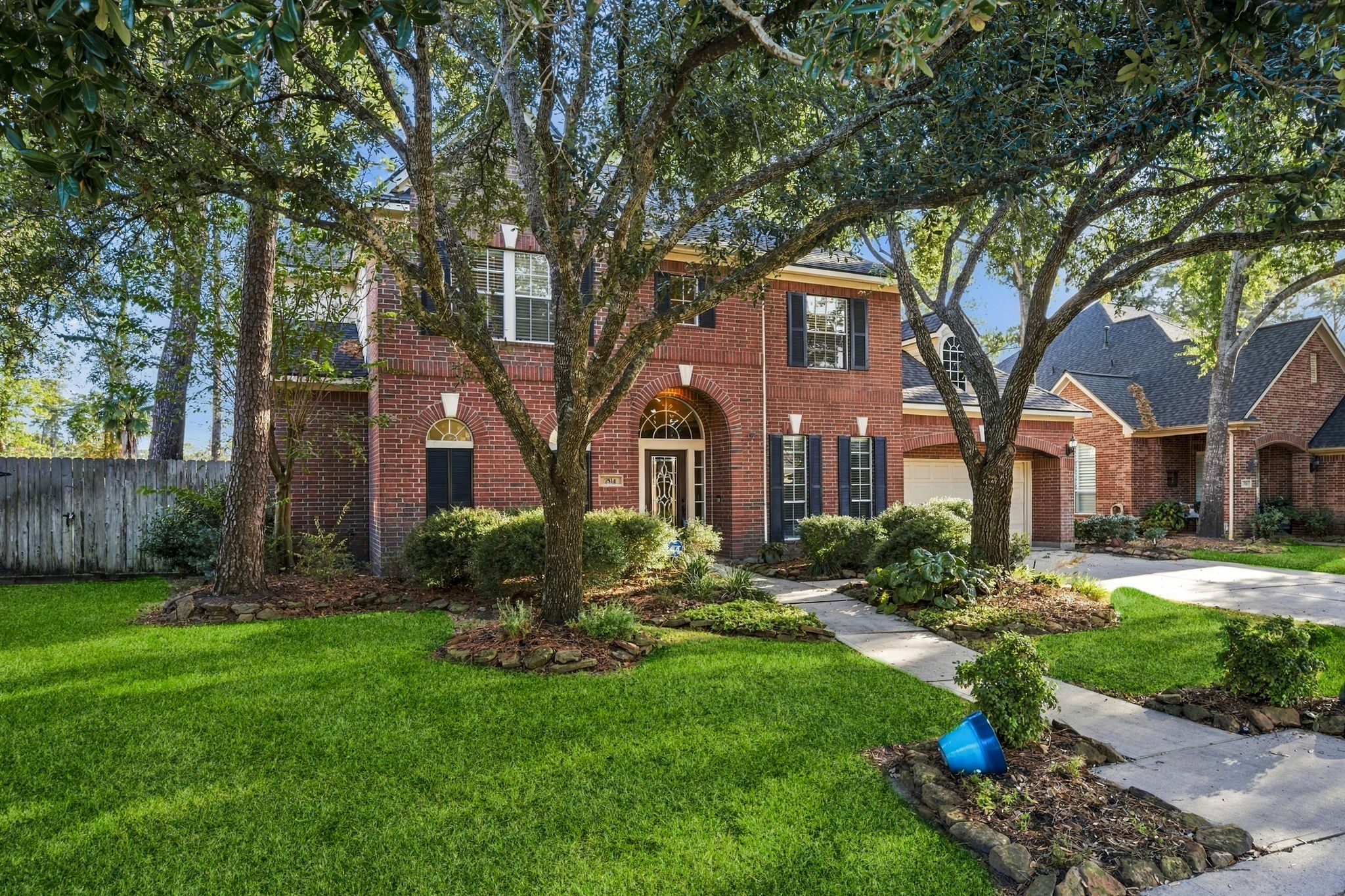 Charming two-story brick home with mature trees and lush landscaping, offering great curb appeal and a welcoming entrance.