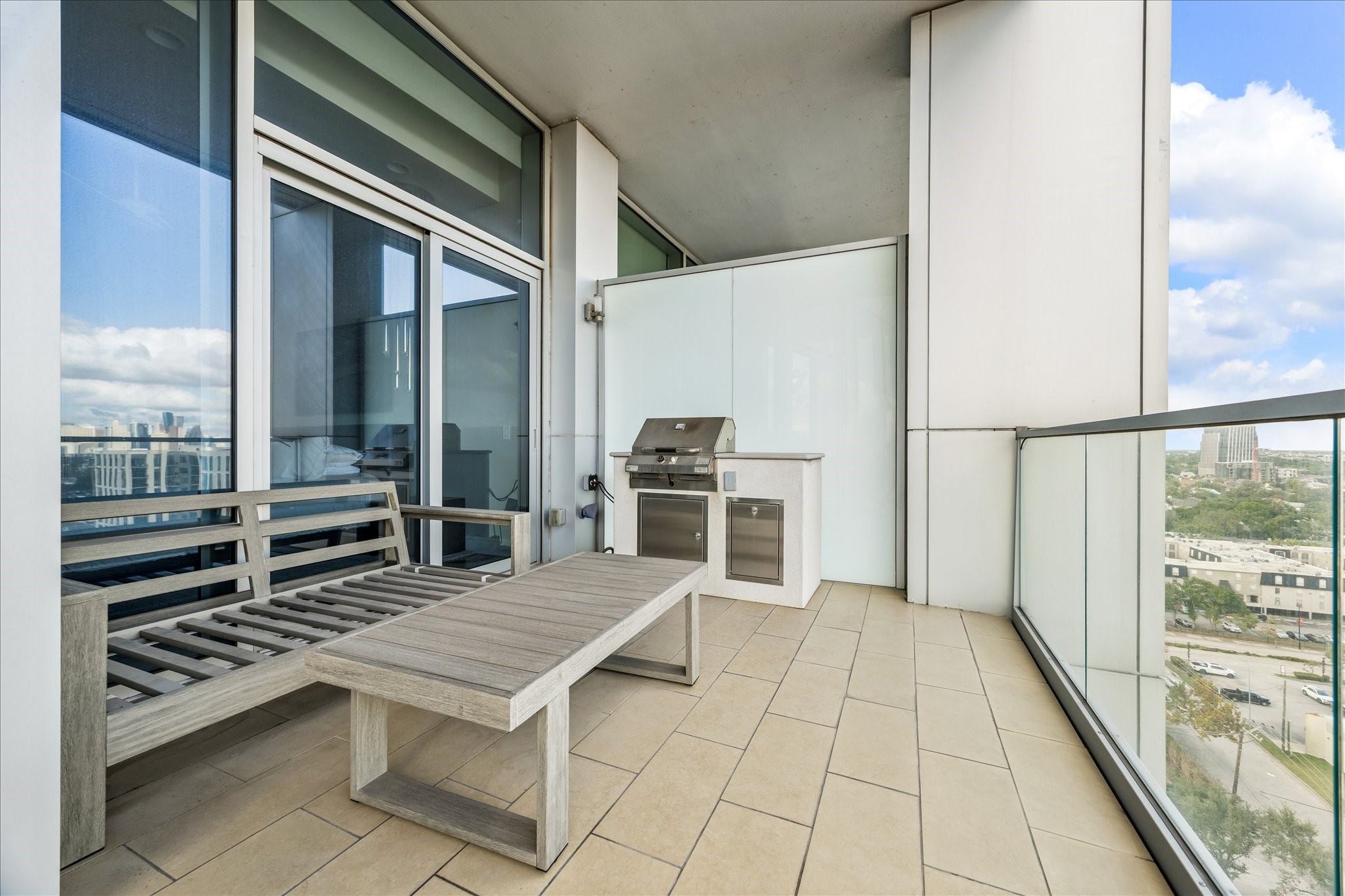 Covered terrace with tile flooring, built-in grill station, and glass railing overlooking the city.