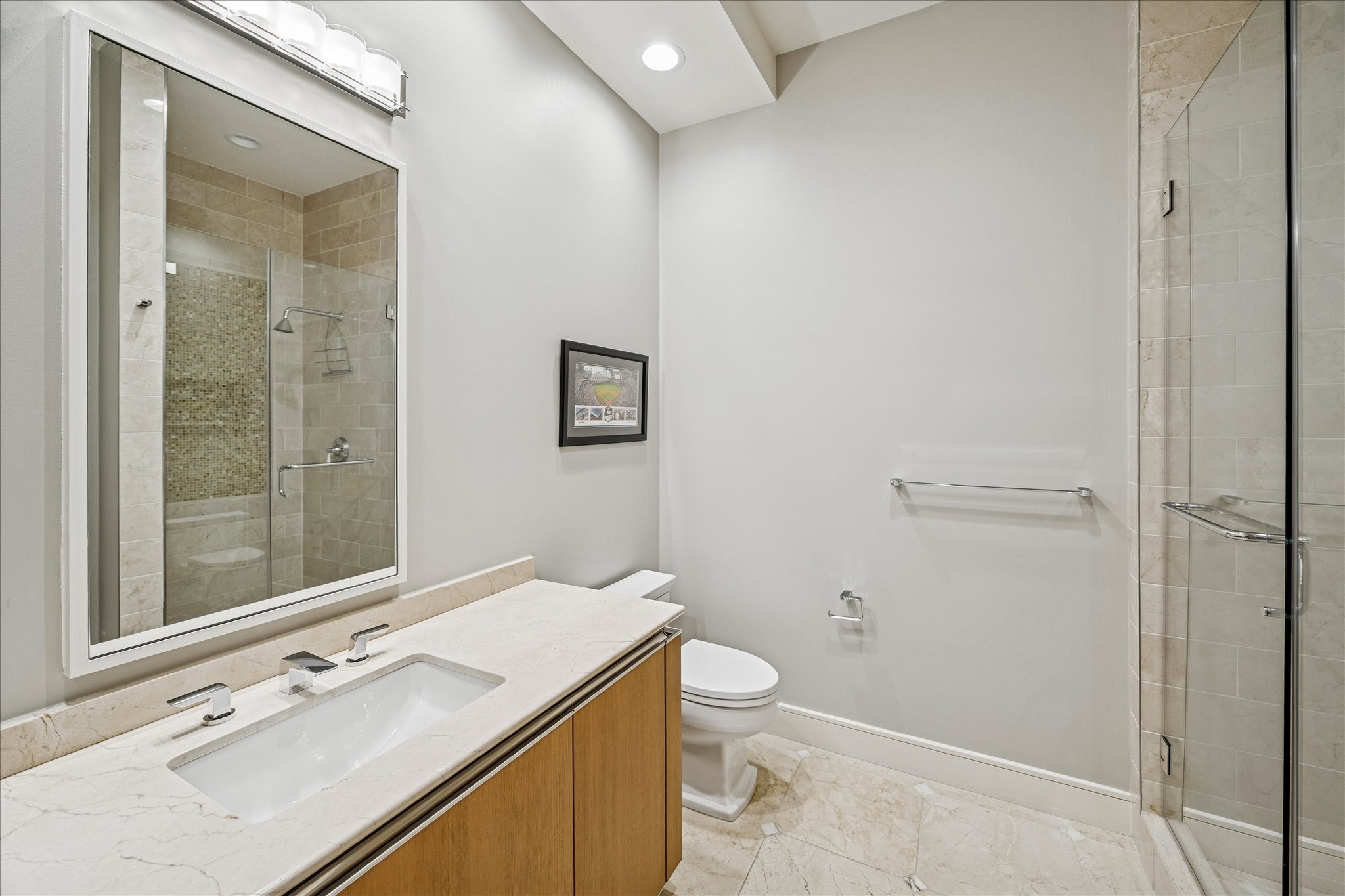 Secondary bathroom with stone vanity, frameless glass shower, and tile flooring.