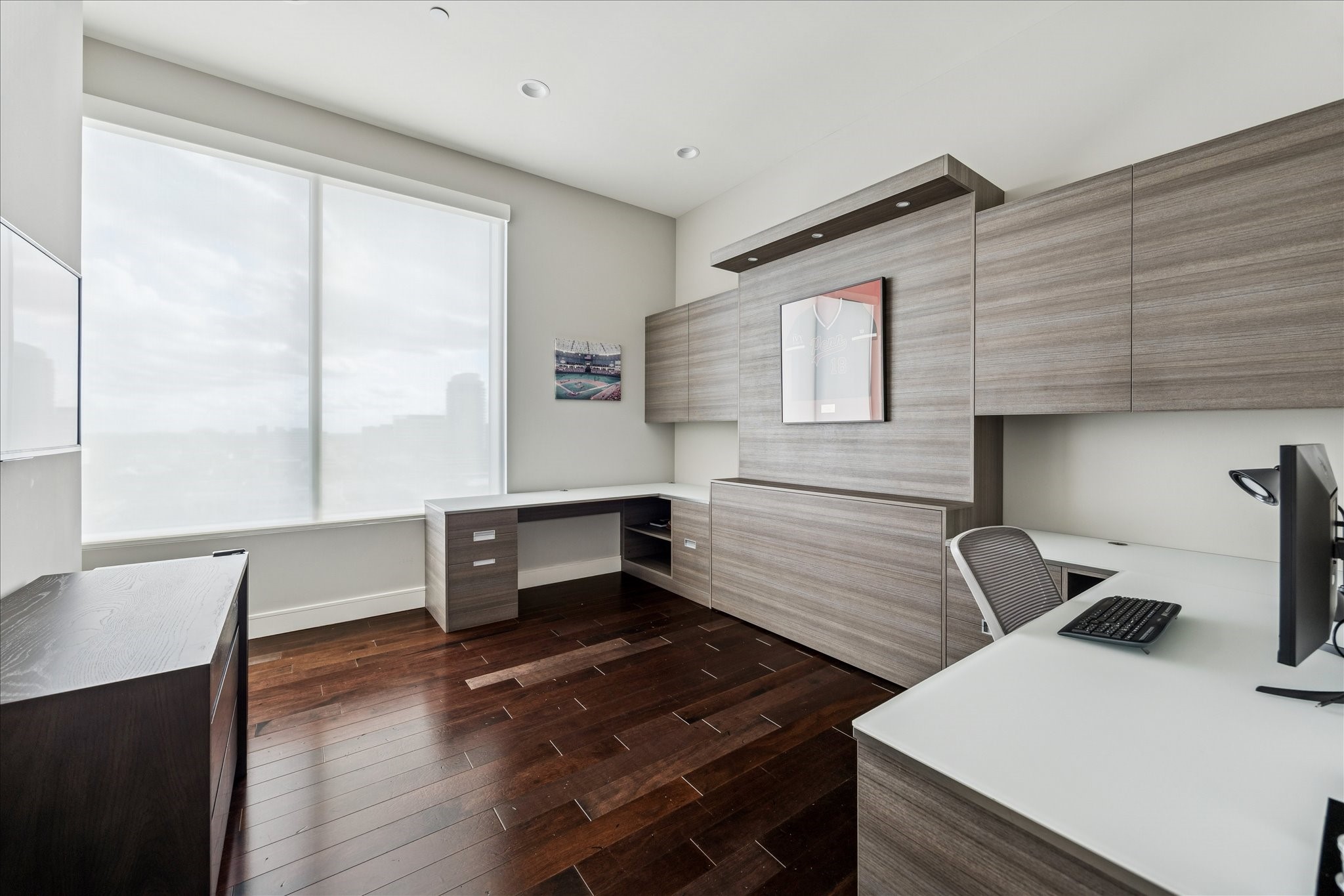Flexible room with custom built-in cabinetry, large window with natural light, hardwood floors, and recessed lighting.