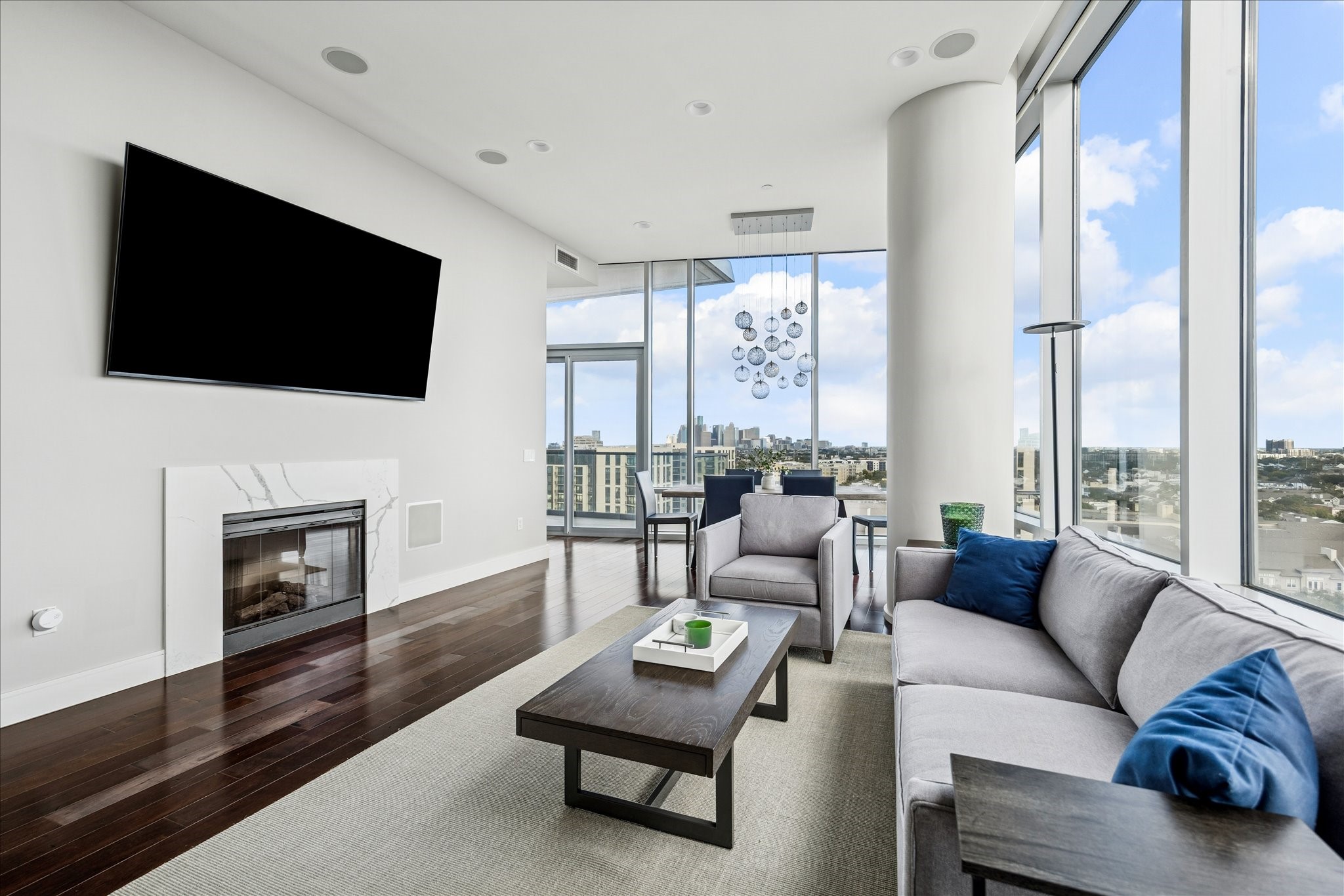 Living area with fireplace and stone surround, recessed lighting, and large picture windows showcasing city views.