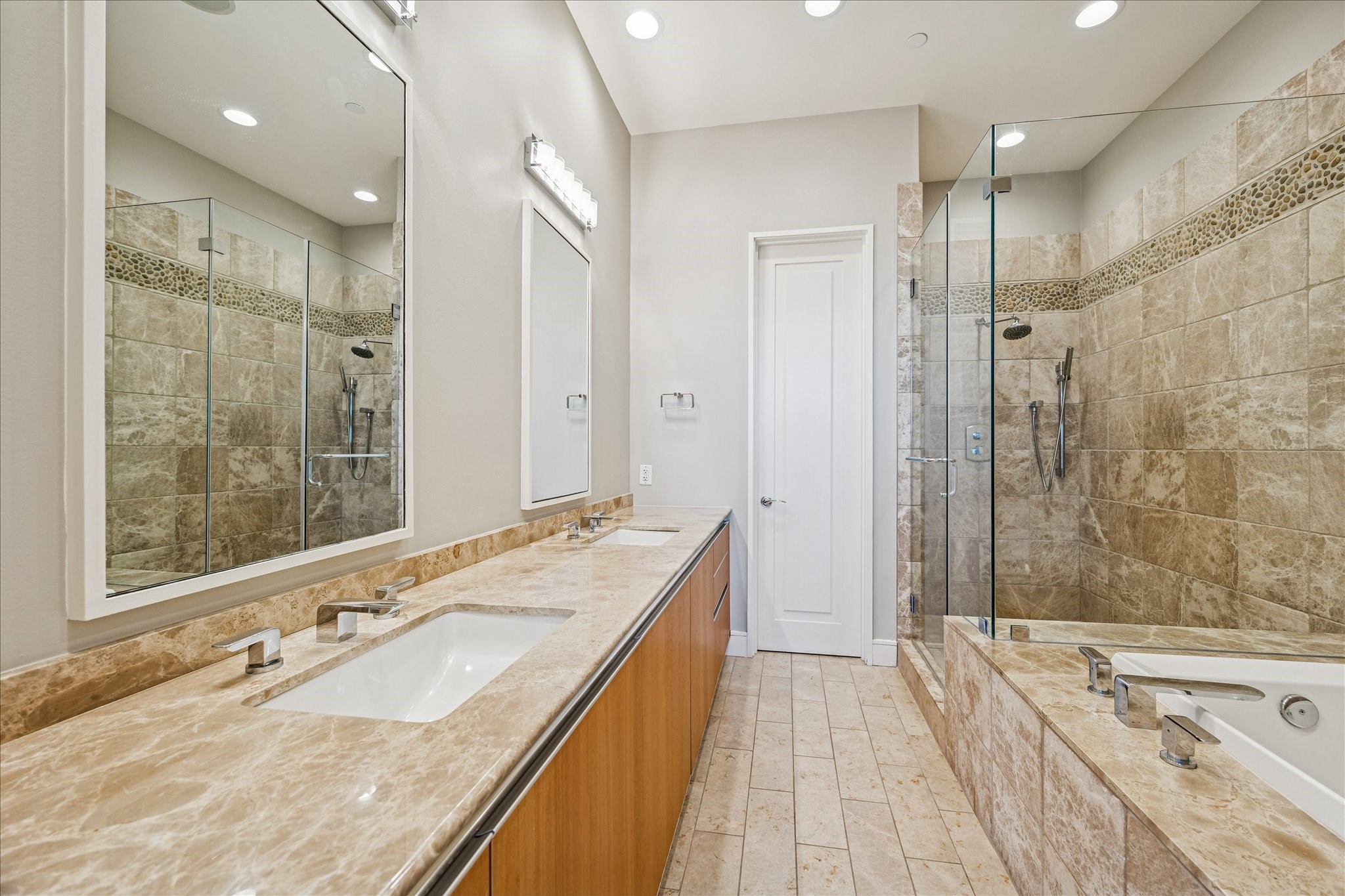 Primary bathroom with dual vanities, stone countertops, glass-enclosed shower, soaking tub, and tile flooring.