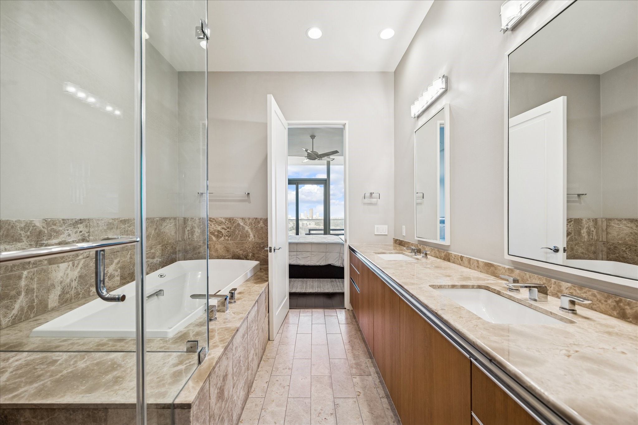 Primary bathroom with dual vanities, stone countertops, glass-enclosed shower, and soaking tub with tile surround.
