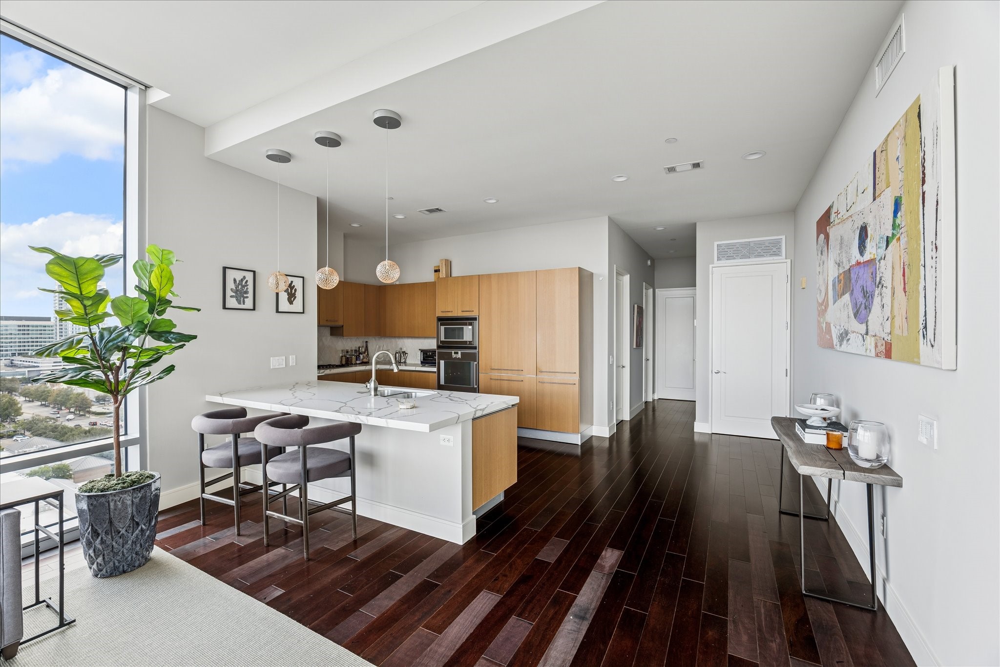 Wide view showcasing kitchen island, hardwood floors, recessed lighting, flat-panel cabinetry, and hallway access to bedrooms.