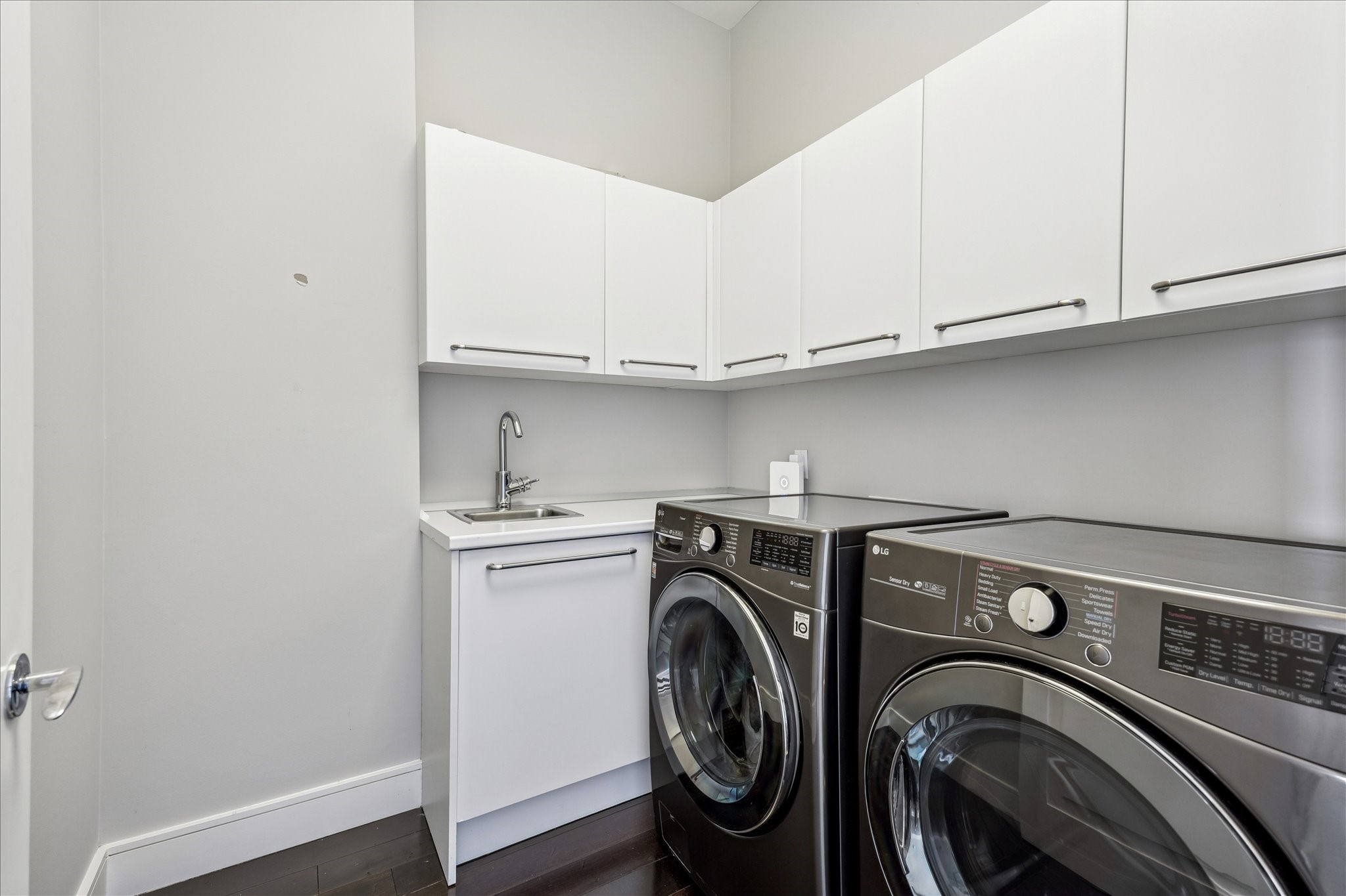 Utility room with upper cabinetry, utility sink, and full-size washer/dryer connections.