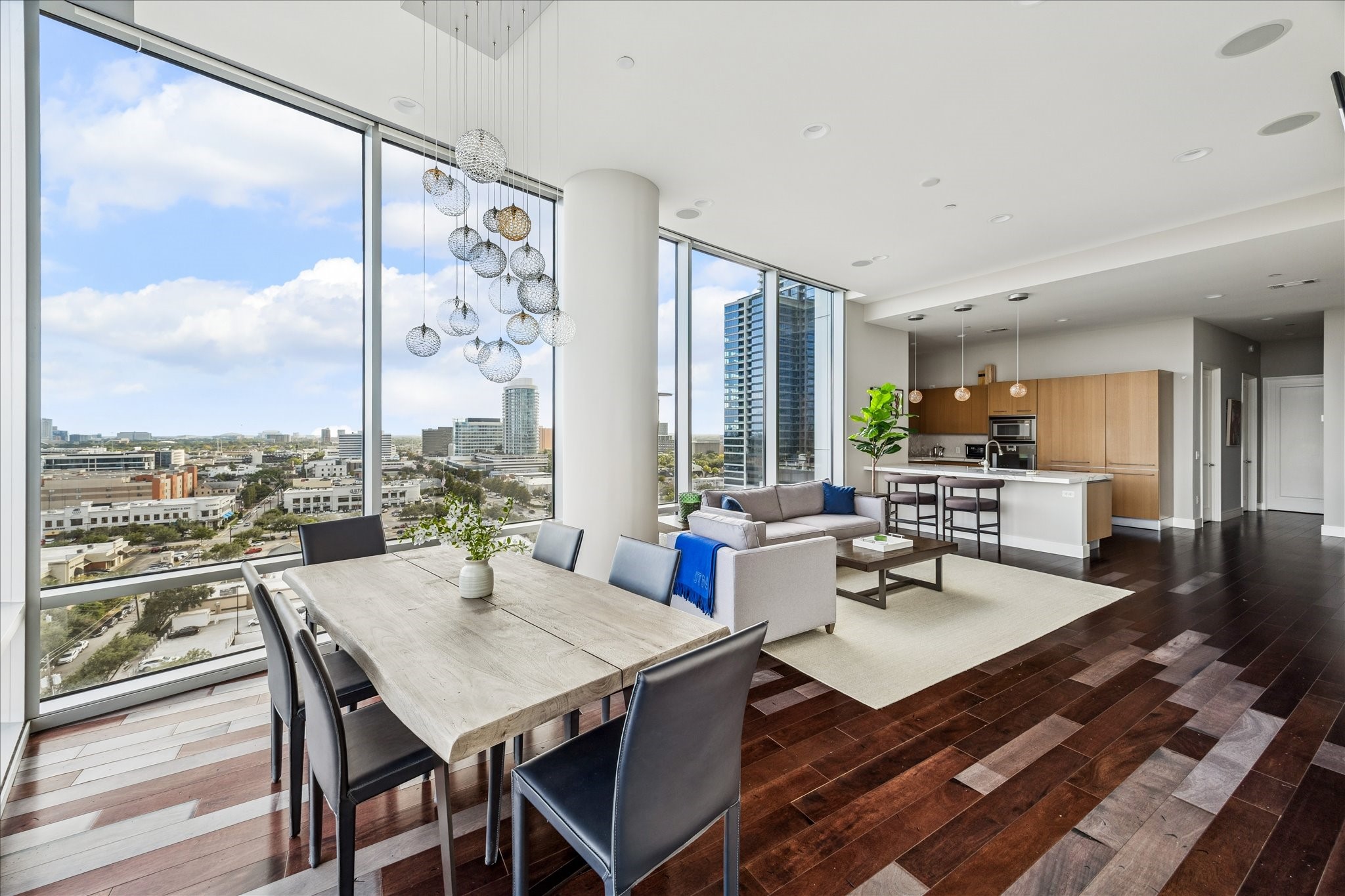 Open-concept living and dining area framed by floor-to-ceiling windows, dark hardwood floors, and expansive city views.