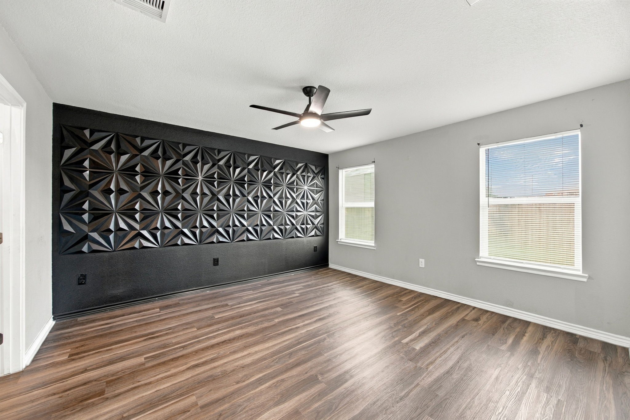 Bedroom featuring a striking geometric black accent wall, modern ceiling fan, wood-look flooring, and natural light.