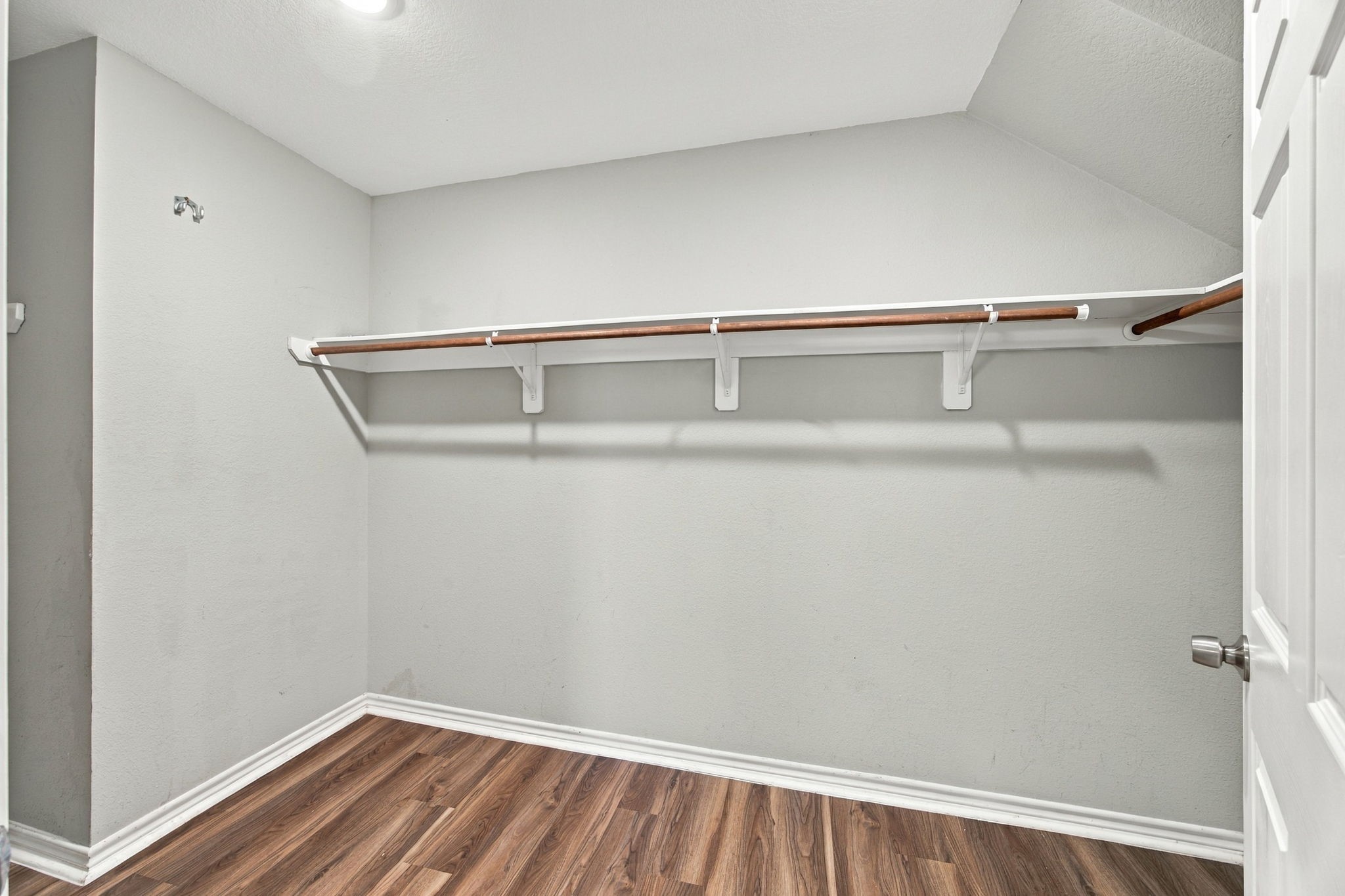 Walk-in closet featuring built-in hanging rods, open storage space, and wood-look flooring for convenient organization.