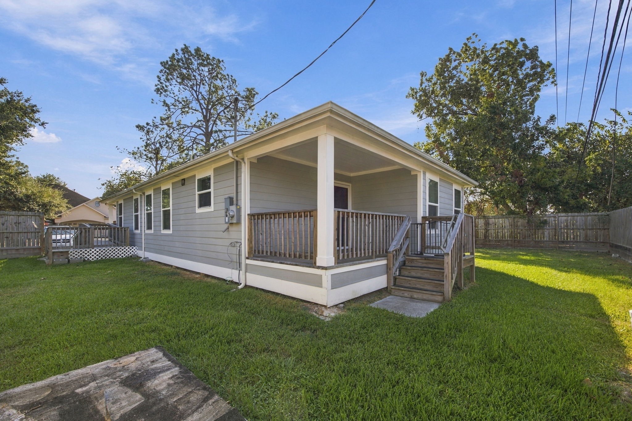 Rear exterior view highlighting the covered porch, wooden deck, fenced backyard, and landscaped lawn.