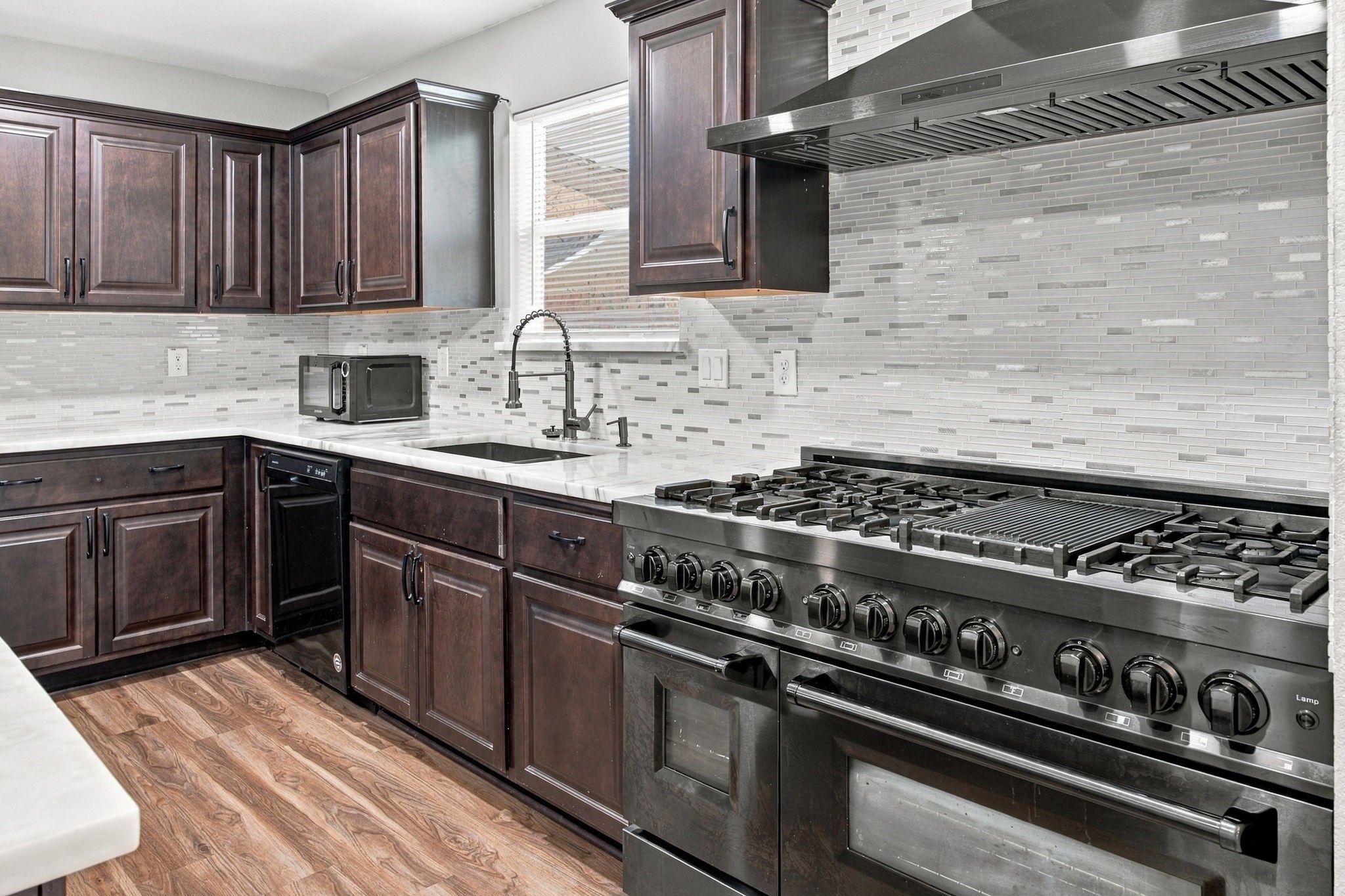 Updated kitchen featuring dark cabinetry, marble-look countertops, a center island, and a large stainless-steel gas range.