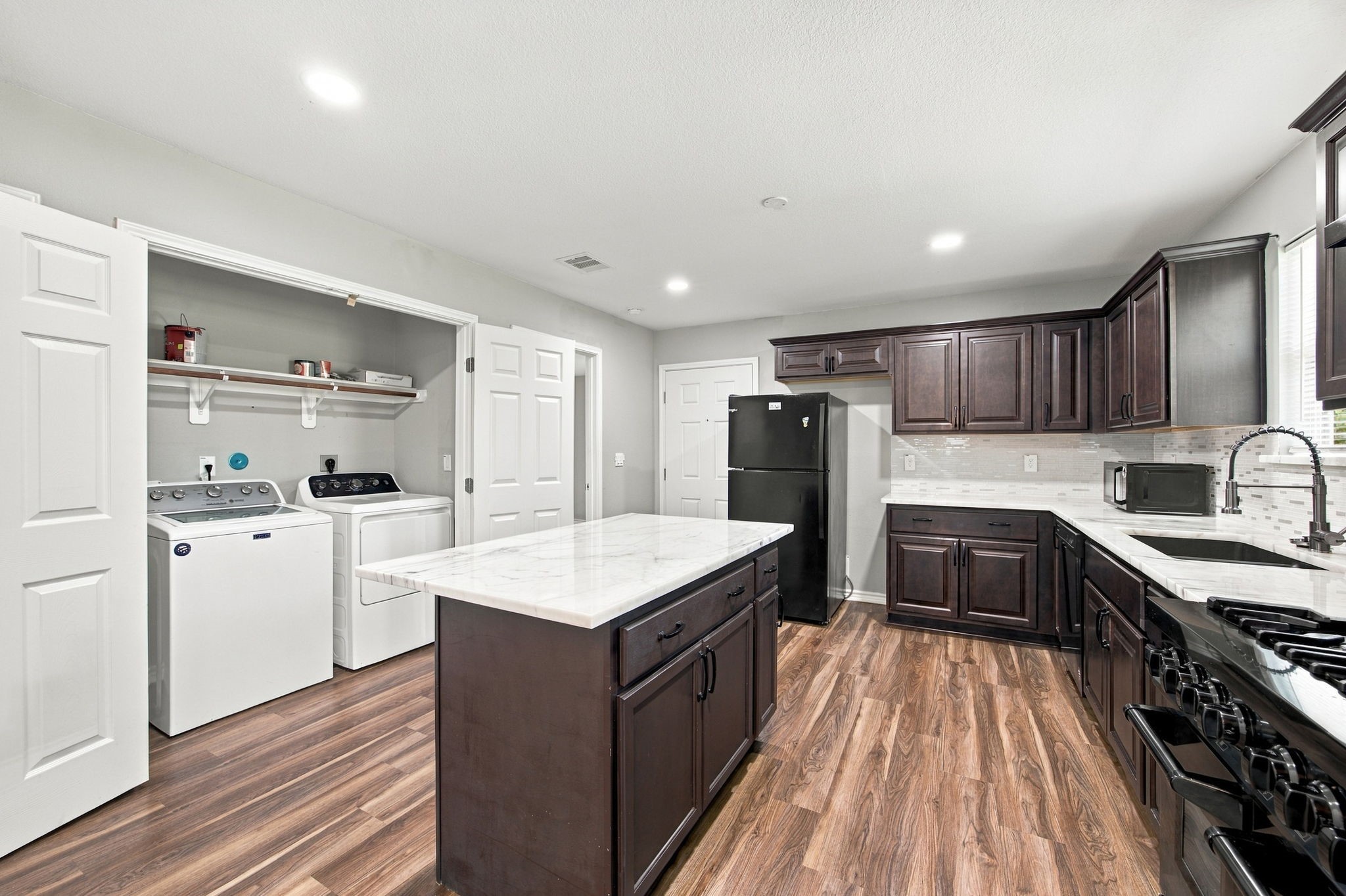 Spacious kitchen with a center island, marble-look countertops, dark cabinetry, gas range, and a convenient in-kitchen laundry area.