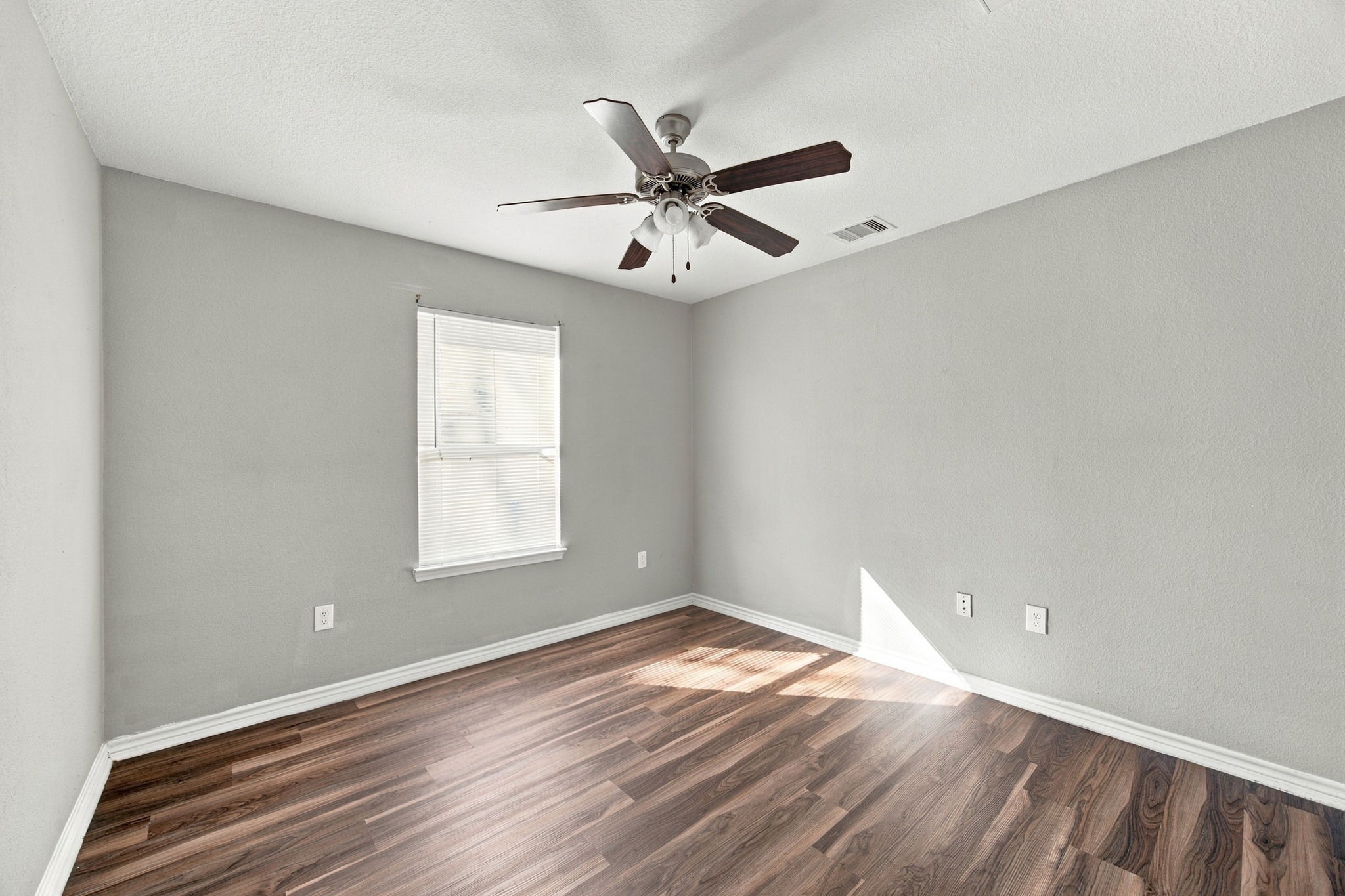 Spacious bedroom featuring wood-look flooring, neutral finishes, a ceiling fan, and a window with blinds.