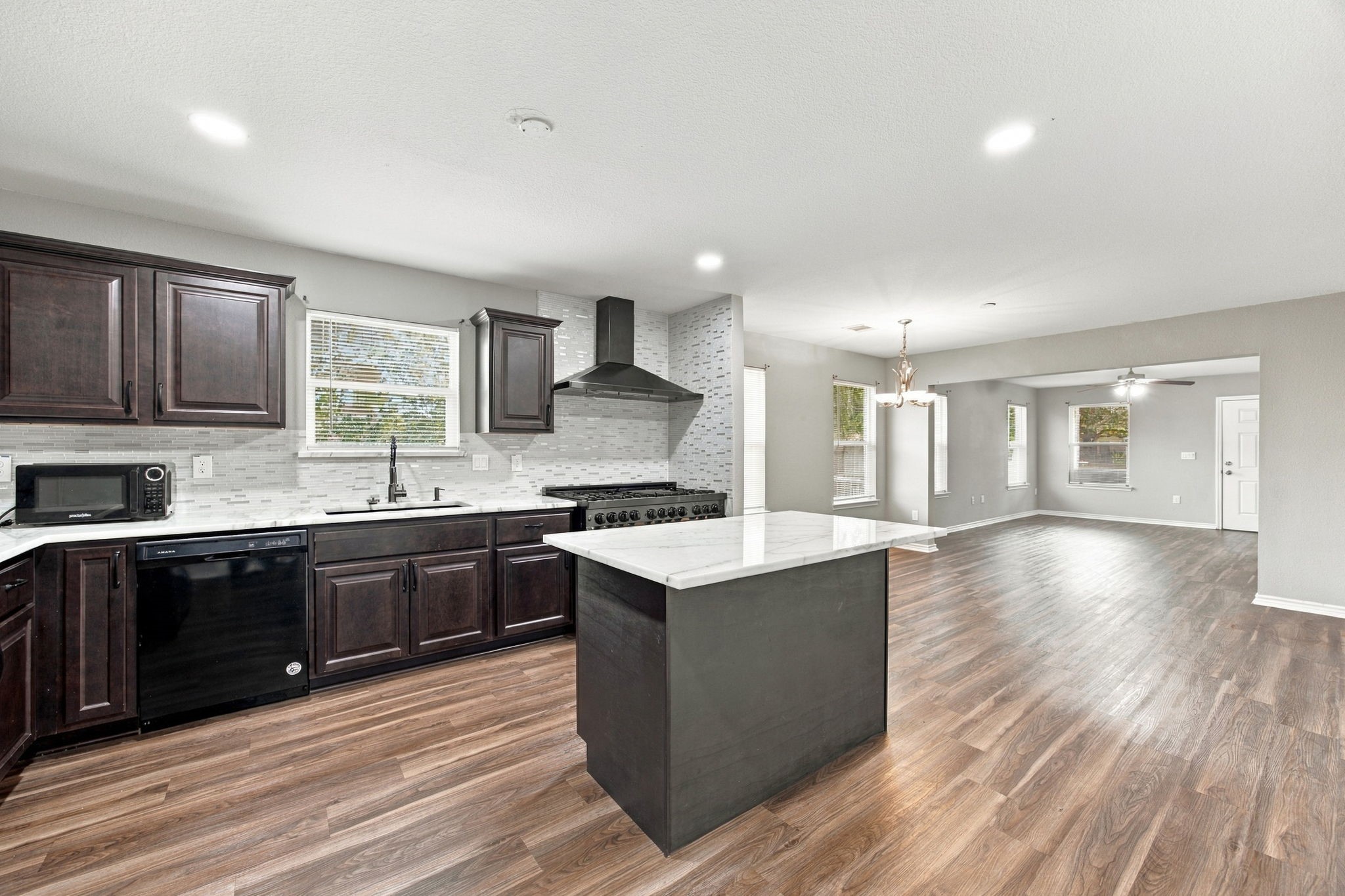 Open-concept kitchen and living area showcasing a large center island, dark cabinetry, stainless steel appliances, and wood-look flooring.