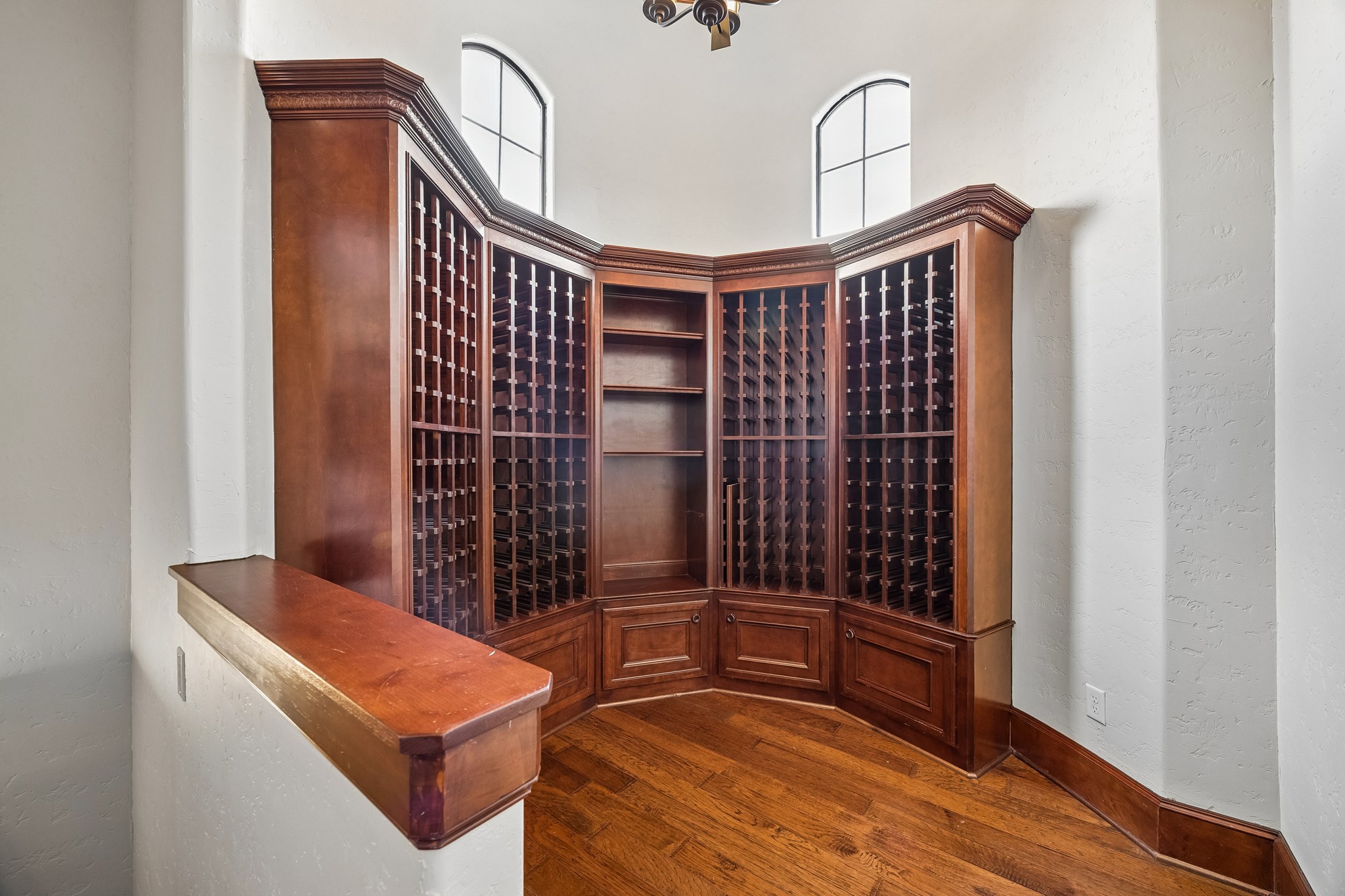 Elegant wine storage room featuring custom wooden cabinetry with ample shelving and natural light from arched windows, perfect for showcasing your collection. There is a back staircase that leads to the garage.