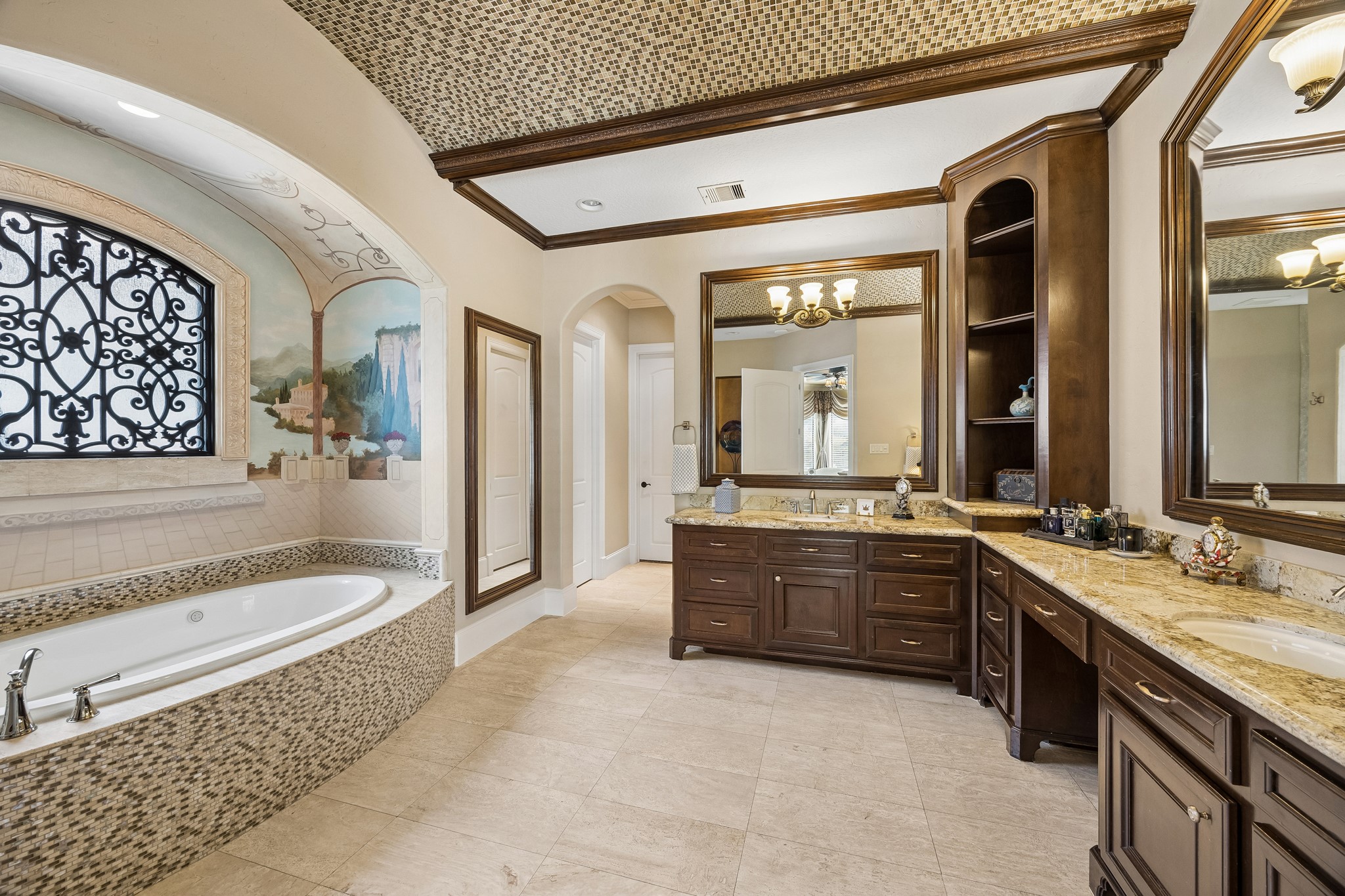 Luxurious bathroom featuring a spacious soaking tub with intricate tile work, elegant dual vanities with rich wood cabinetry, and a beautifully detailed barrel vaulted ceiling.