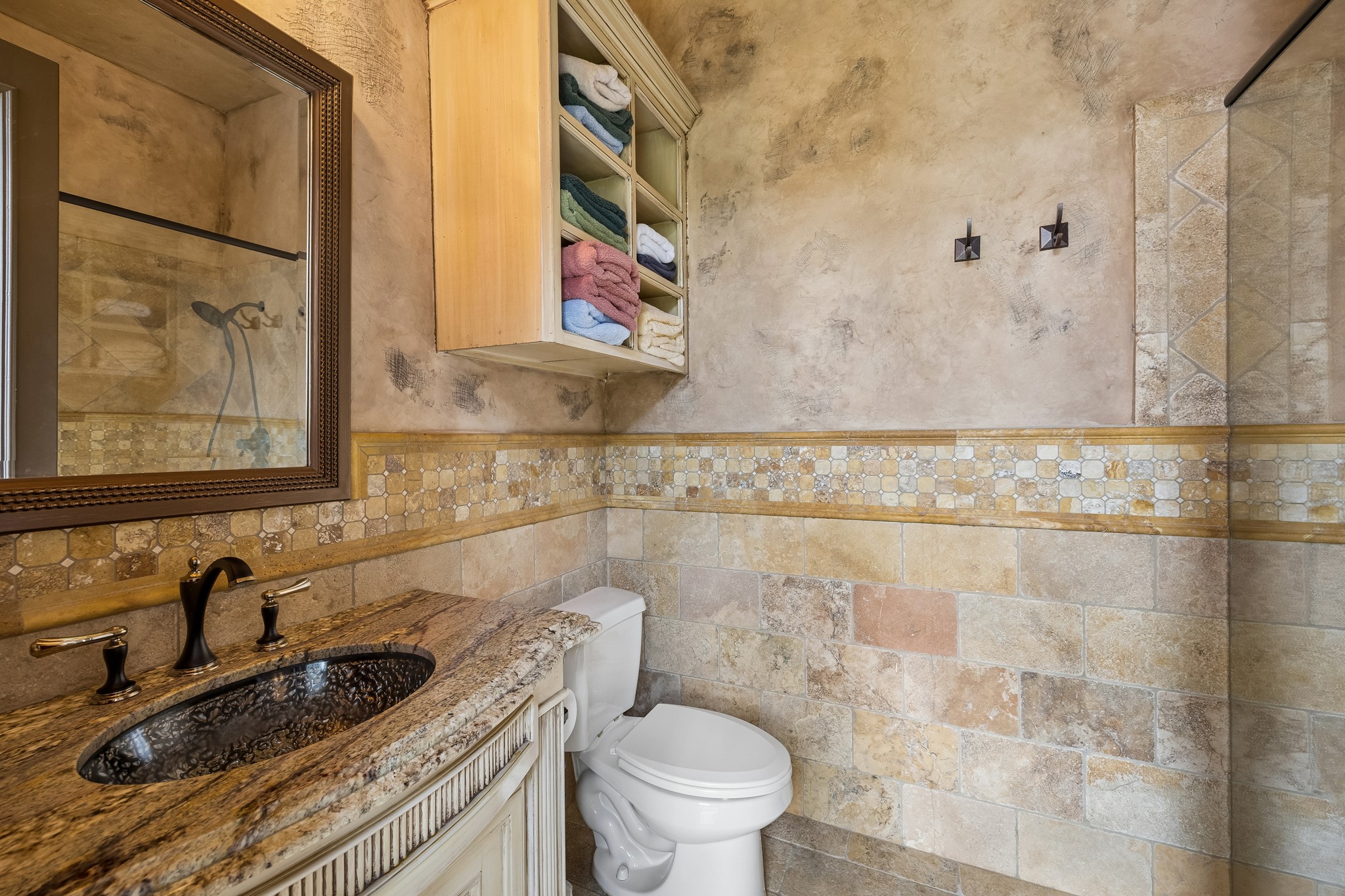 Elegant pool bathroom featuring a granite countertop, intricate tile work, and a spacious shower area, perfectly situated adjacent to the sauna.