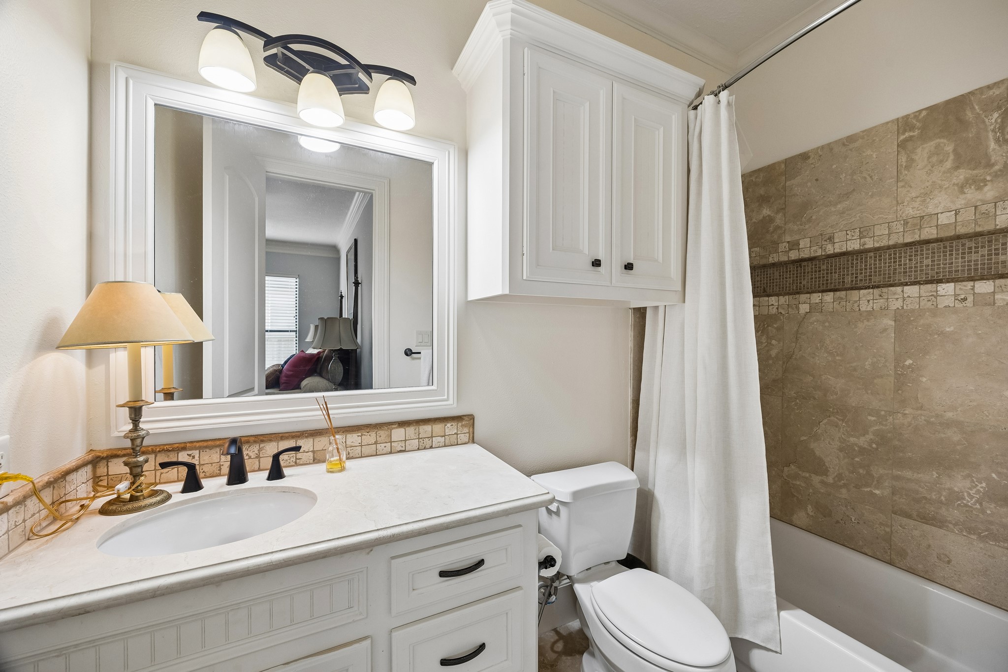 Charming en-suite bathroom featuring a sleek vanity with a marble countertop, elegant lighting, and a tiled shower with a classic curtain for a timeless look.