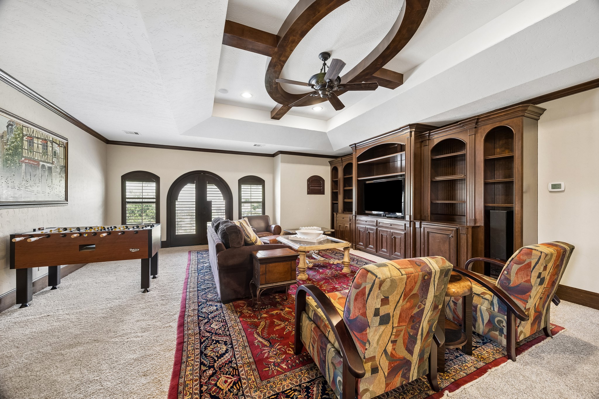 Spacious second floor game room featuring a multiple seating areas and custom built-in cabinetry, all under a beautifully detailed ceiling with a central fan.