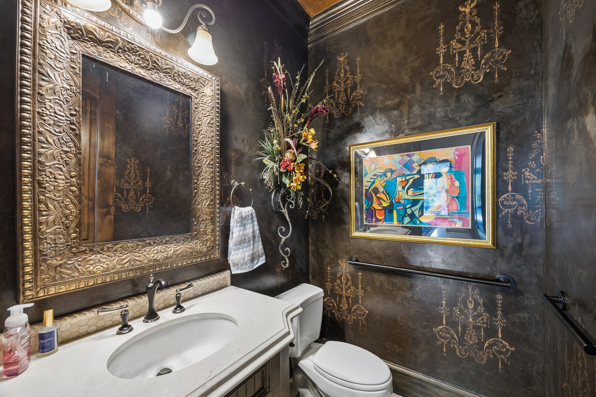 Luxurious powder room featuring elegant dark walls with gold accents, an ornate framed mirror, and vibrant artwork, creating a sophisticated ambiance. There are two powder rooms for added convenience.