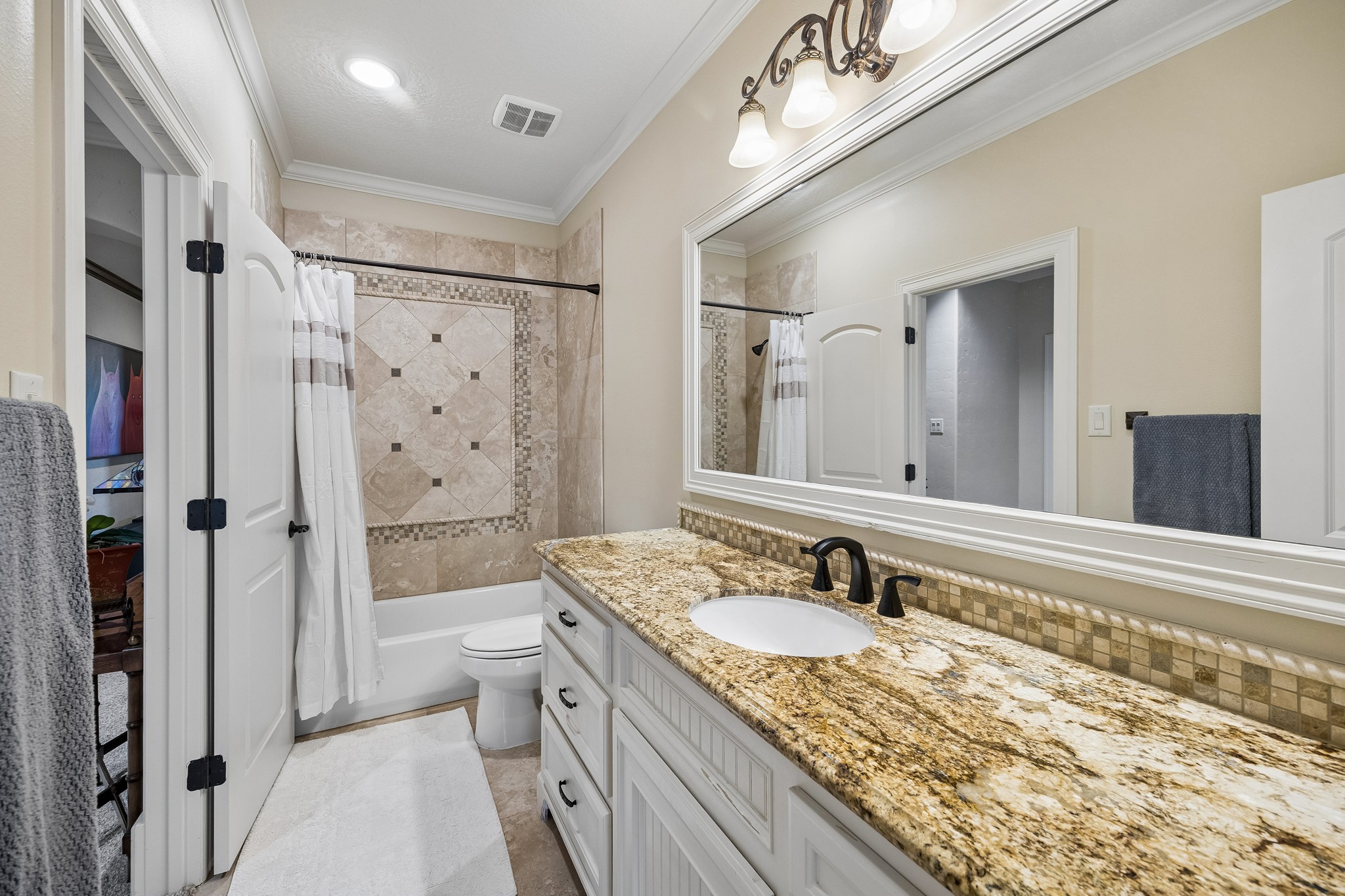 Elegant en-suite bathroom featuring a granite countertop, stylish fixtures, and a beautifully tiled shower area with a decorative inlay.