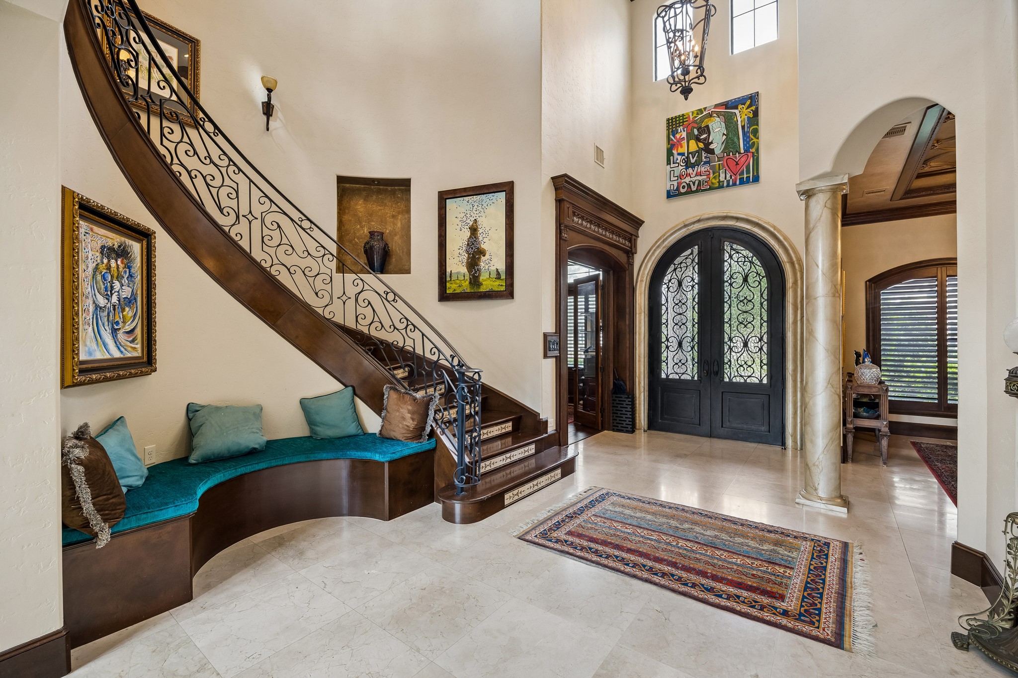 Grand foyer featuring a sweeping staircase with intricate ironwork, elegant custom double doors, and stylish art pieces, complemented by a built-in bench. Grand foyer featuring a sweeping staircase with intricate ironwork, elegant custom double doors, and stylish art pieces, complemented by a built-in bench.