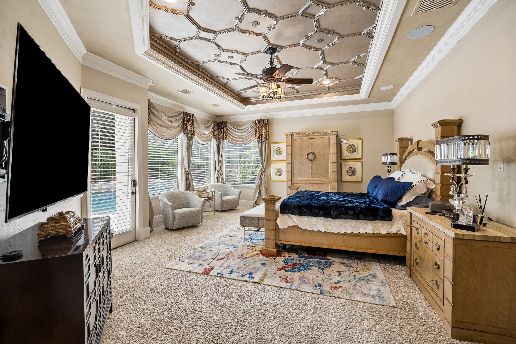 Luxurious primary bedroom featuring a stunning coffered ceiling, sitting area, and large windows offering ample natural light and pool views.