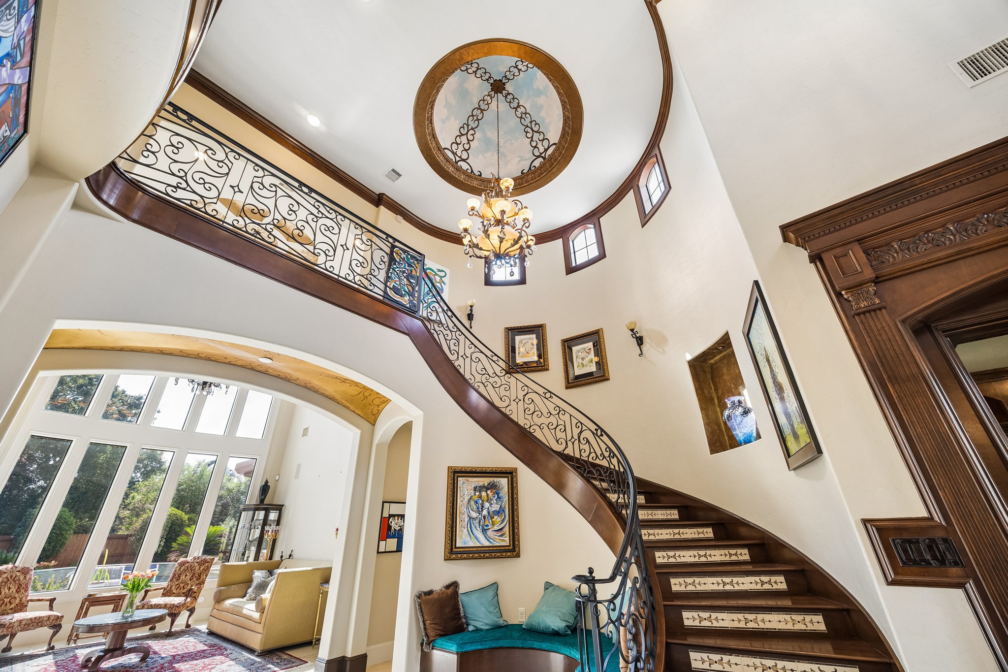 Elegant curved staircase with intricate wrought iron railing, leading to the spacious second floor. Note the beautiful ceiling treatment and chandelier.