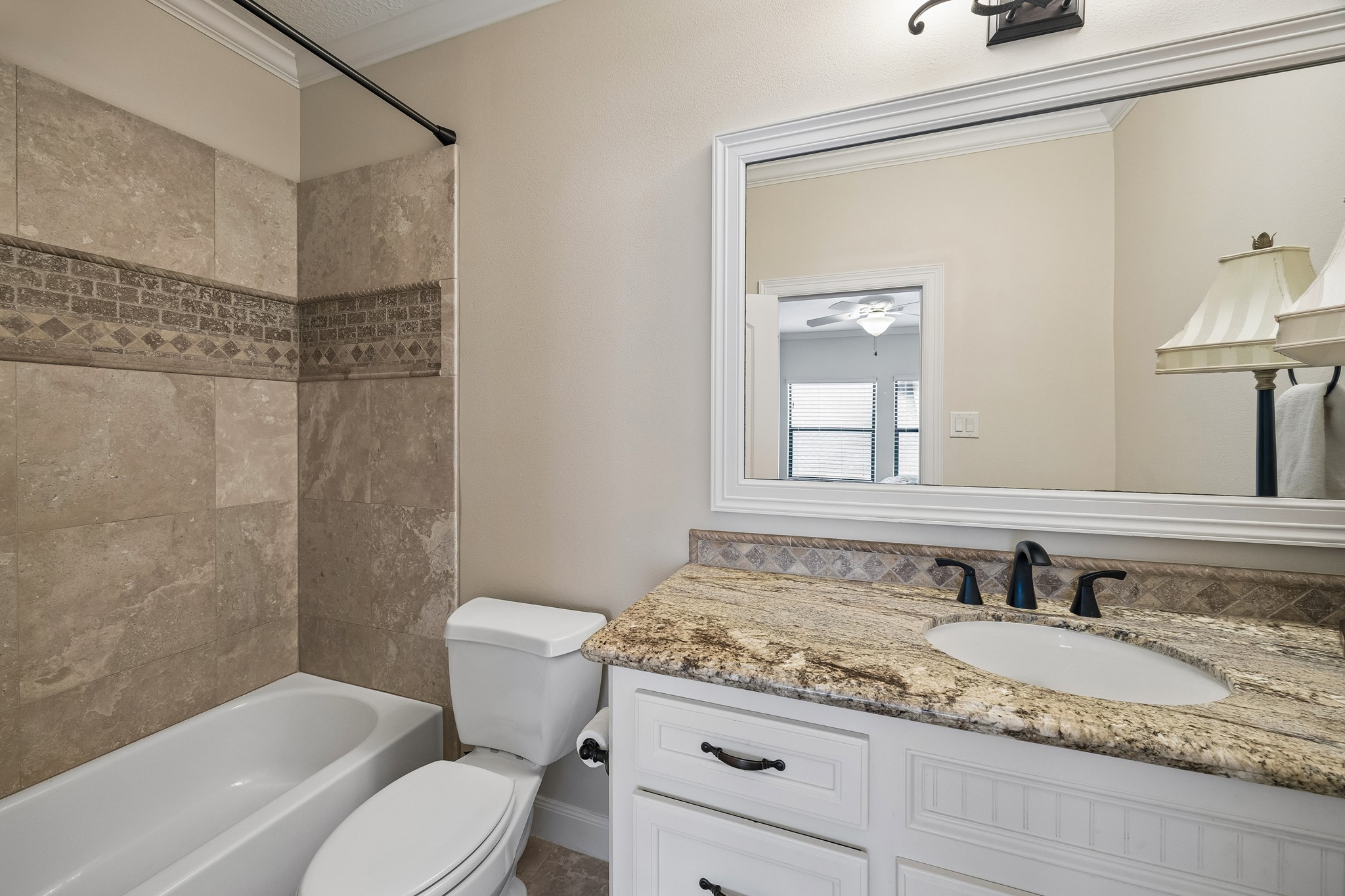 Elegant en-suite bathroom featuring a granite countertop, modern fixtures, and a stylishly tiled shower and bath area.